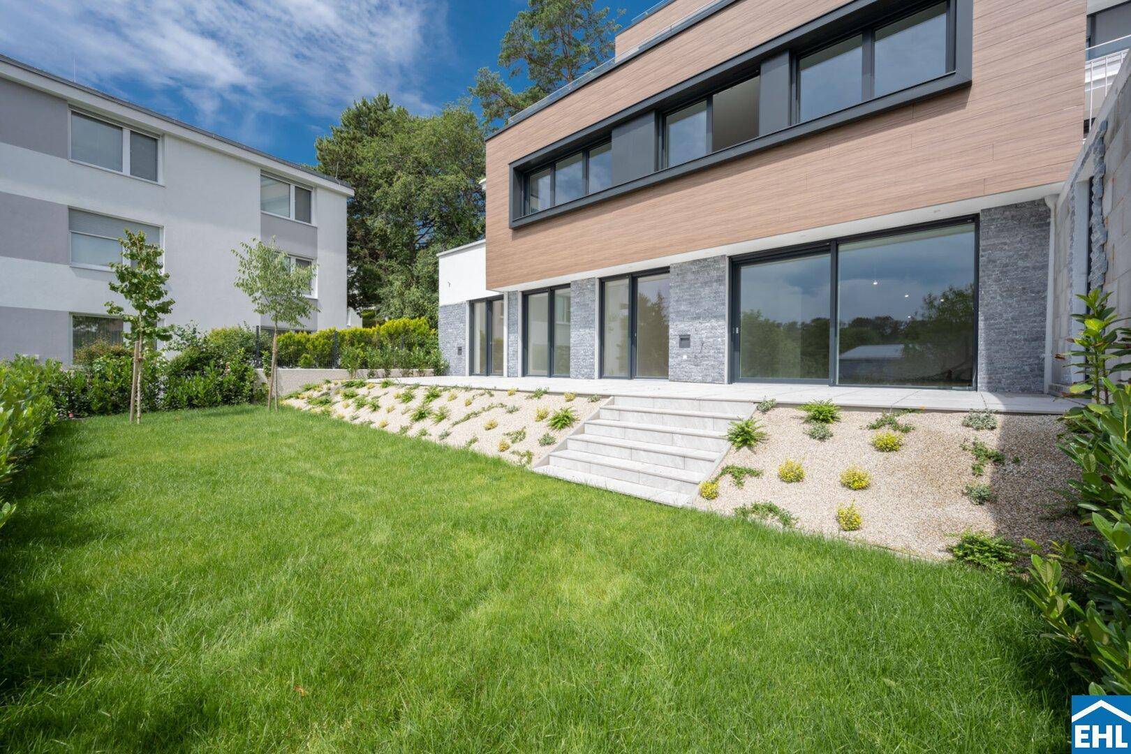 Ansicht des modernen Gebäudes mit gepflegtem Rasen und Steintreppe zum Garten.