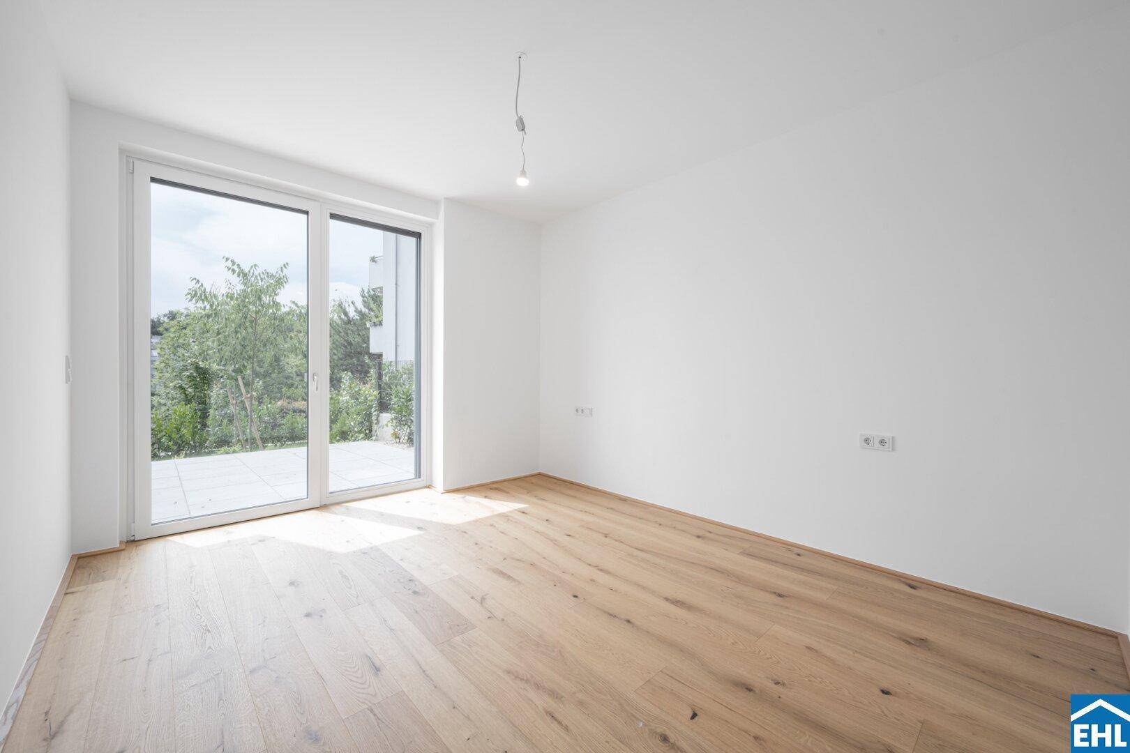 Geräumiger, heller Raum mit Holzboden und Zugang zu einem Außenbereich.