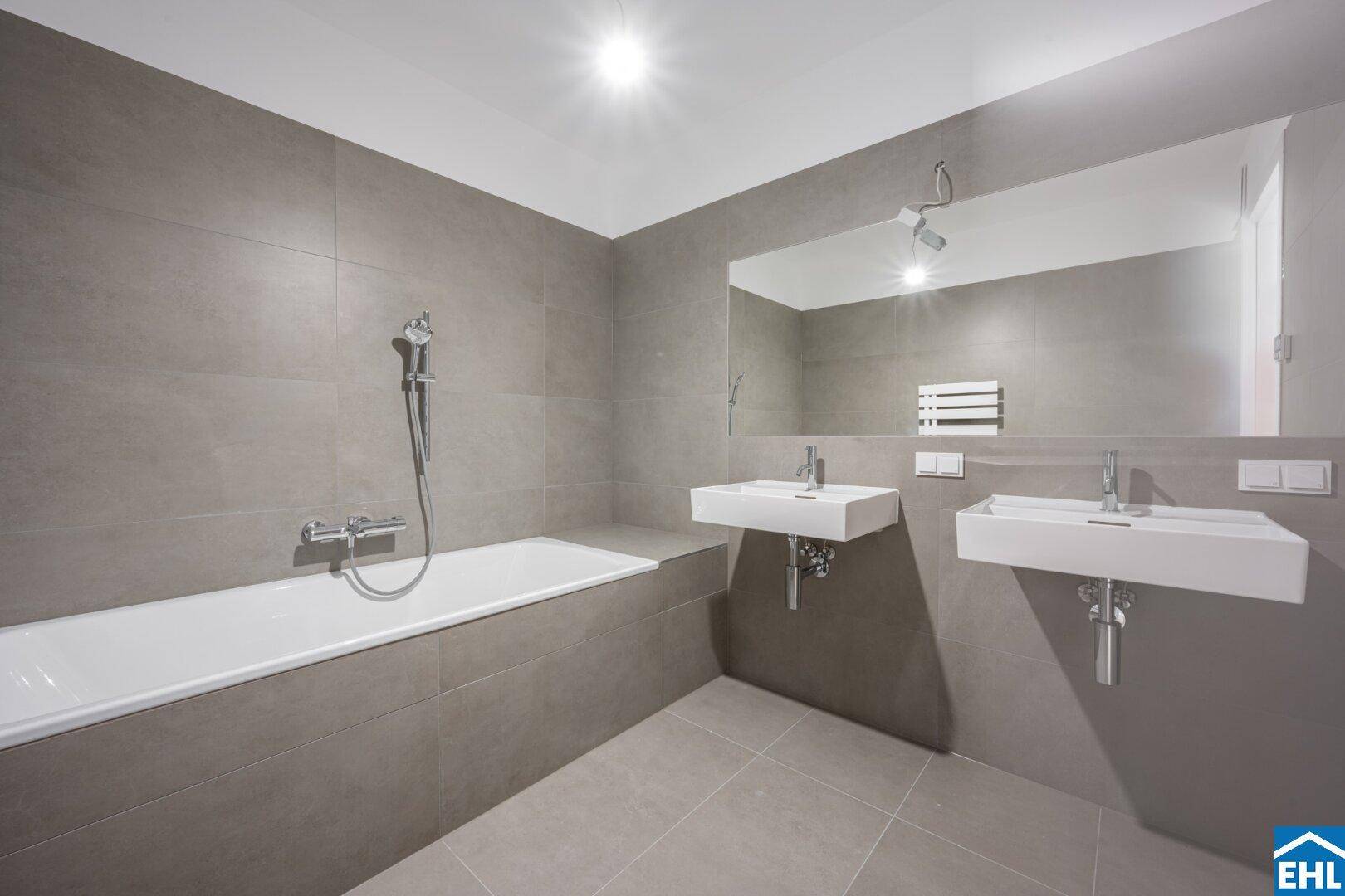 Elegantes Badezimmer mit Badewanne, Doppelwaschbecken und großen grauen Fliesen.