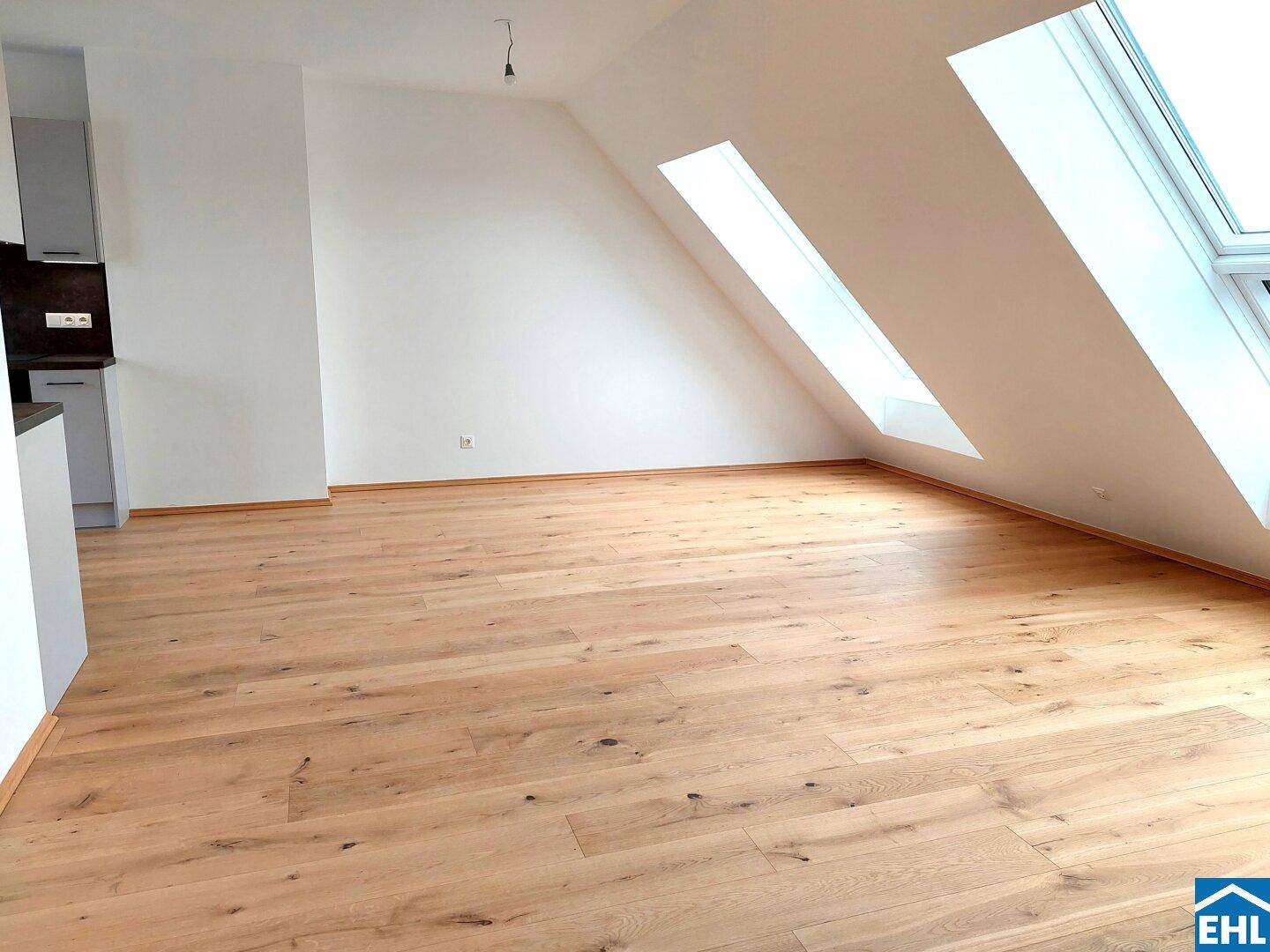 Heller Dachgeschossraum mit Holzboden, Dachfenstern und einer angedeuteten Küchenzeile.