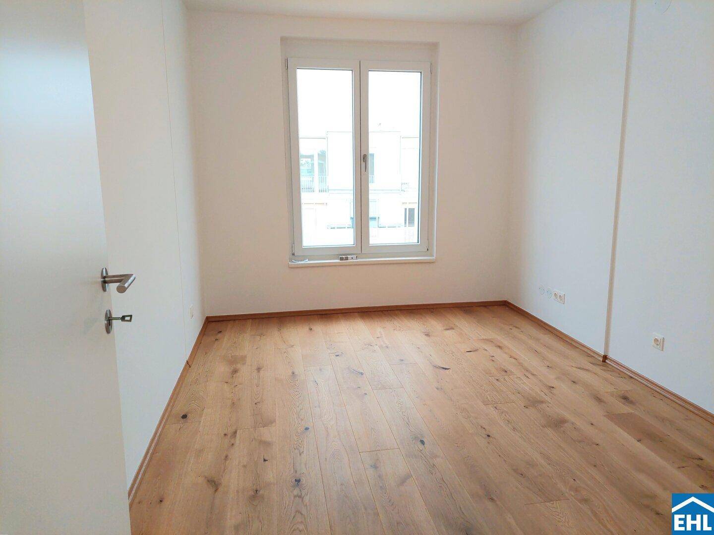 Helles Schlafzimmer mit Holzboden und großem Fenster, bereit zum Einrichten.