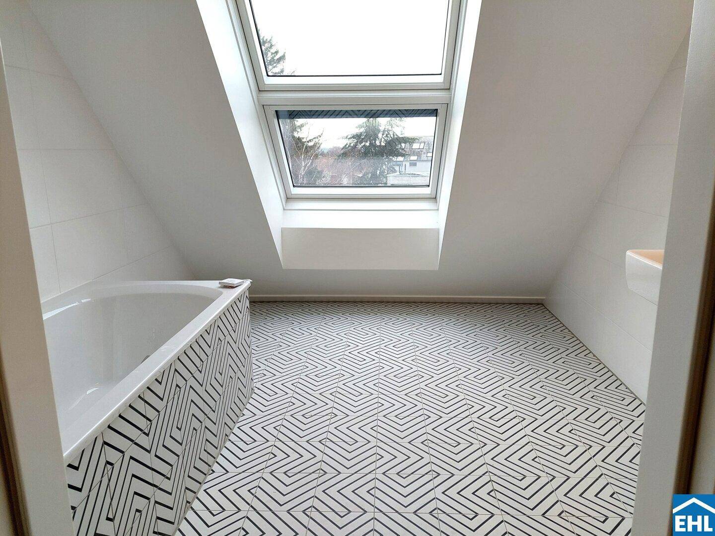 Modernes Badezimmer im Dachgeschoss mit Badewanne, Dachfenster und auffälligen Bodenfliesen.