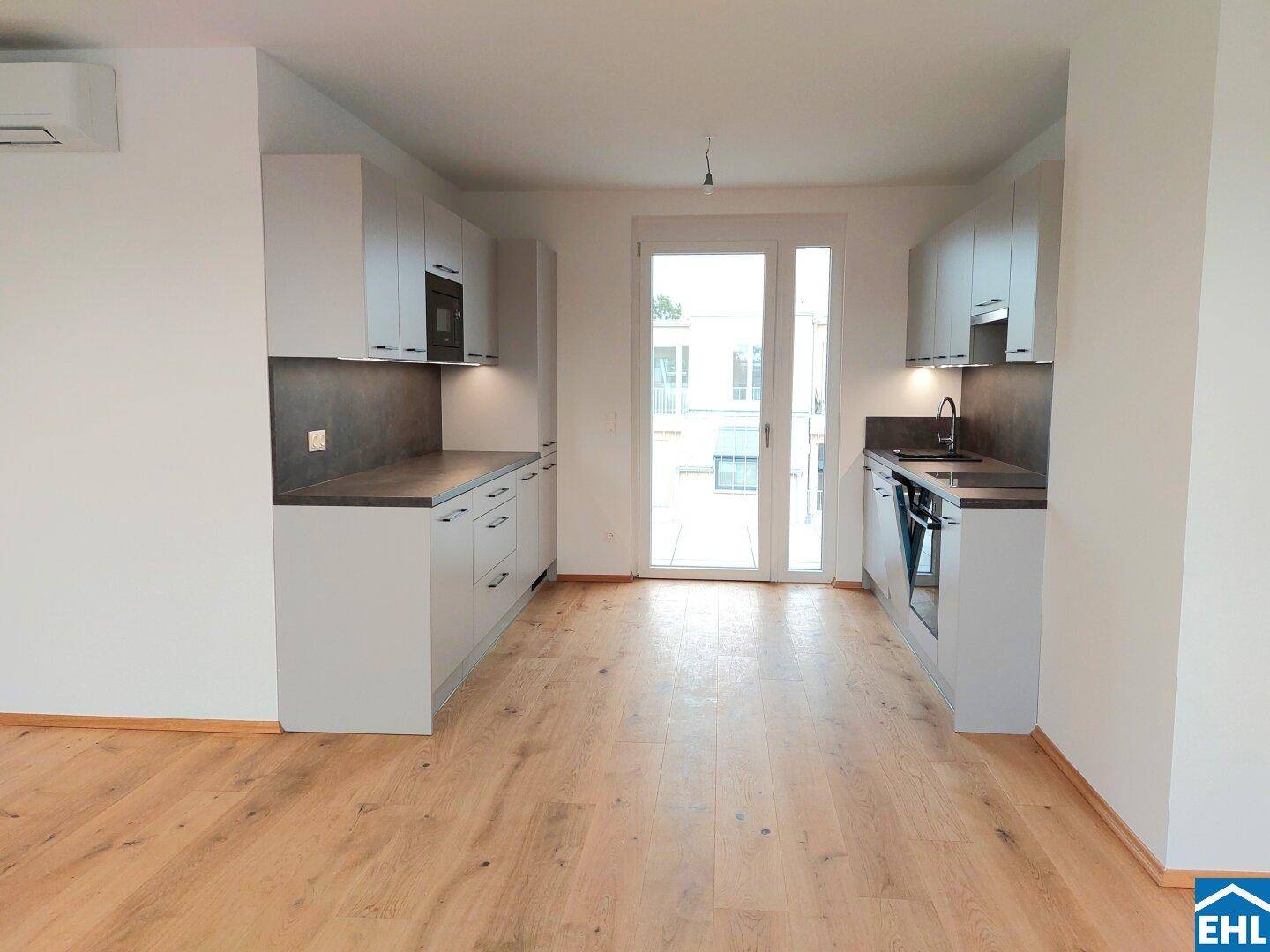 Moderne Küche mit hellgrauen Schränken, Holzboden und Zugang zu einem Außenbereich.