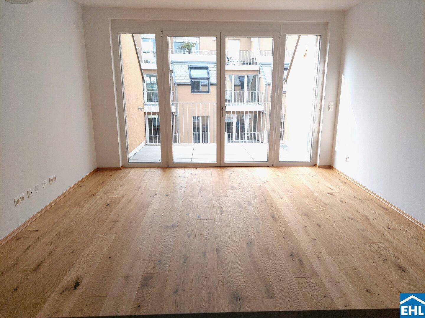 Heller Raum mit Holzboden und Zugang zu einem Balkon, bietet viel Tageslicht und Ausblick.