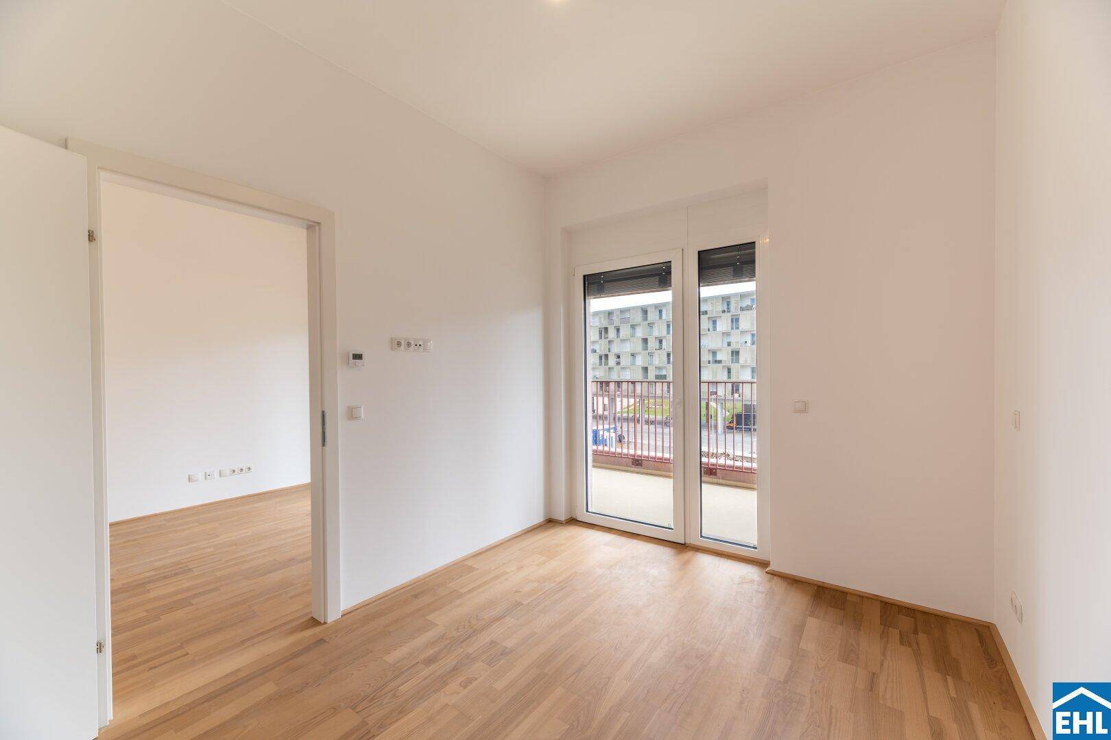 Helles Zimmer mit Parkettboden und Zugang zu einem Balkon, ideal als Schlafzimmer.