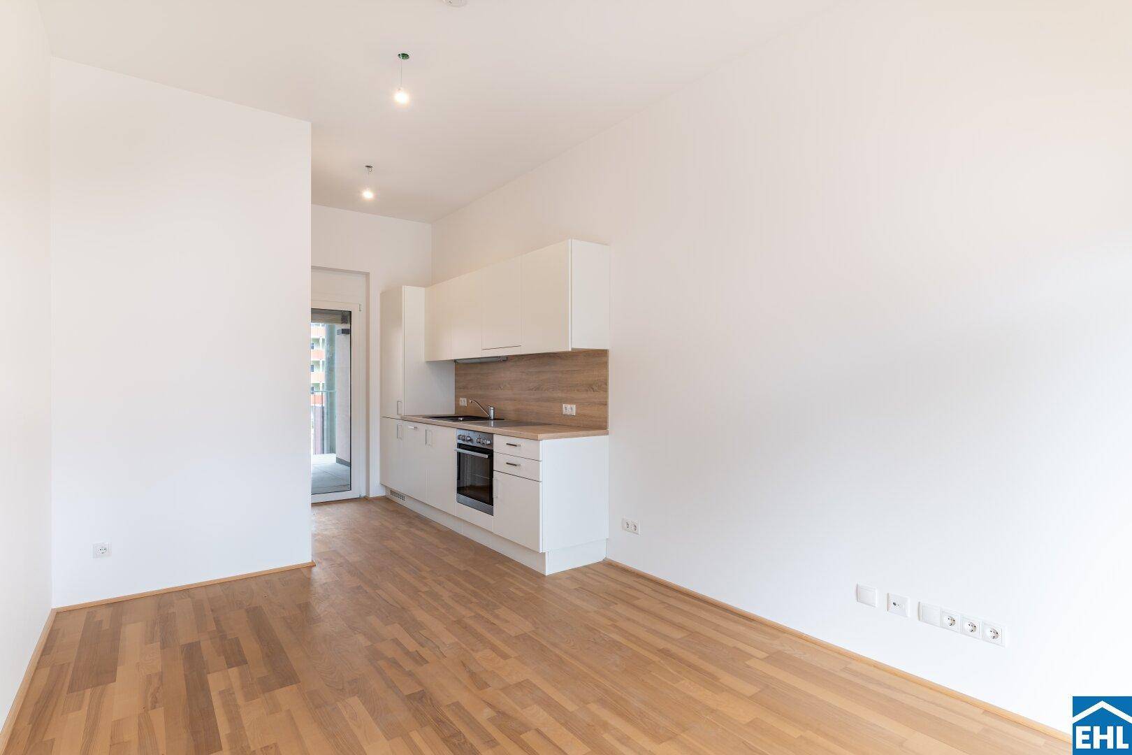 Moderne Einbauküche mit weißen Schränken und Holz-Arbeitsplatte in einem offenen Wohnbereich.