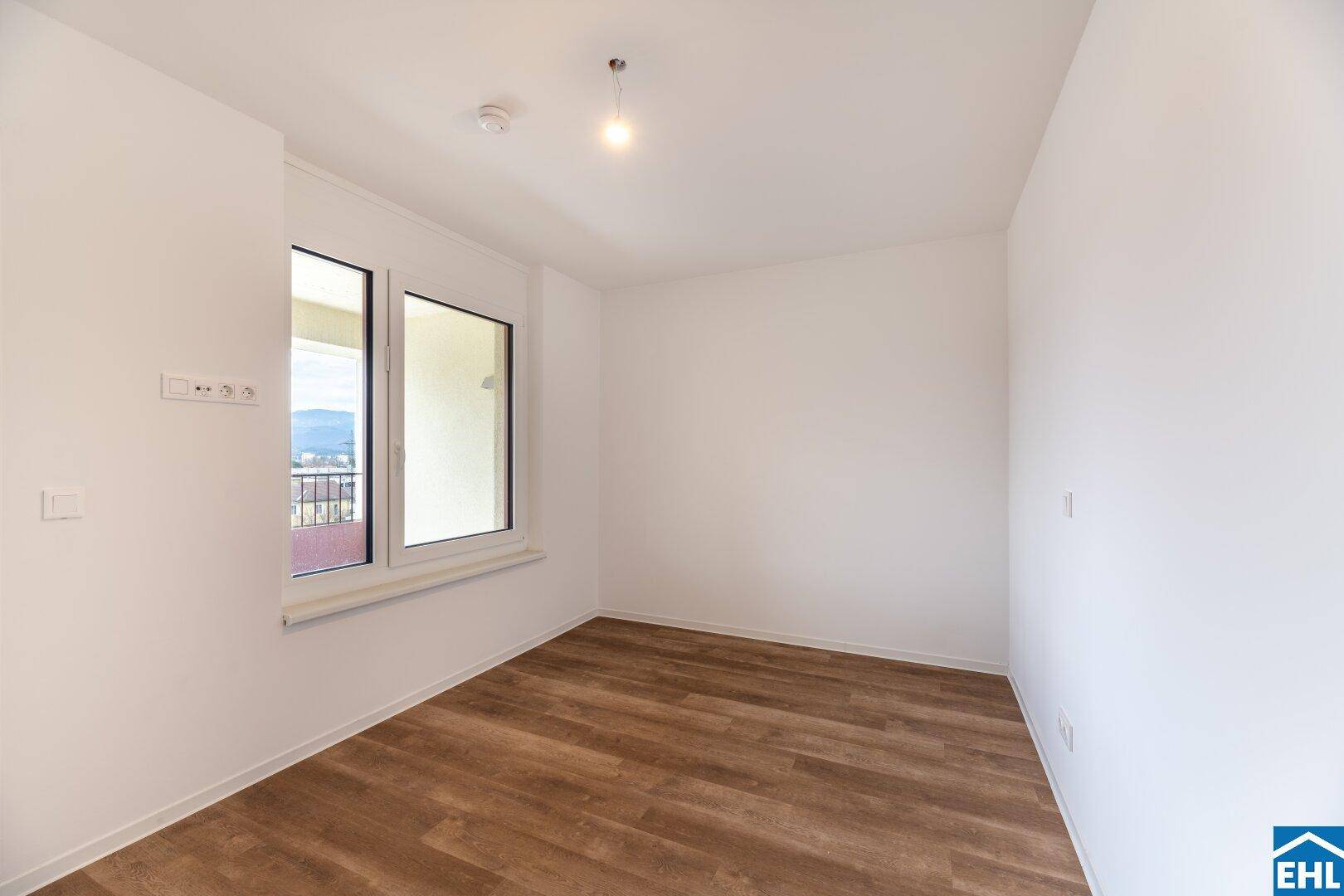 Ruhiges Schlafzimmer mit großen Fenstern und Blick ins Grüne, ausgestattet mit modernem Laminatboden.