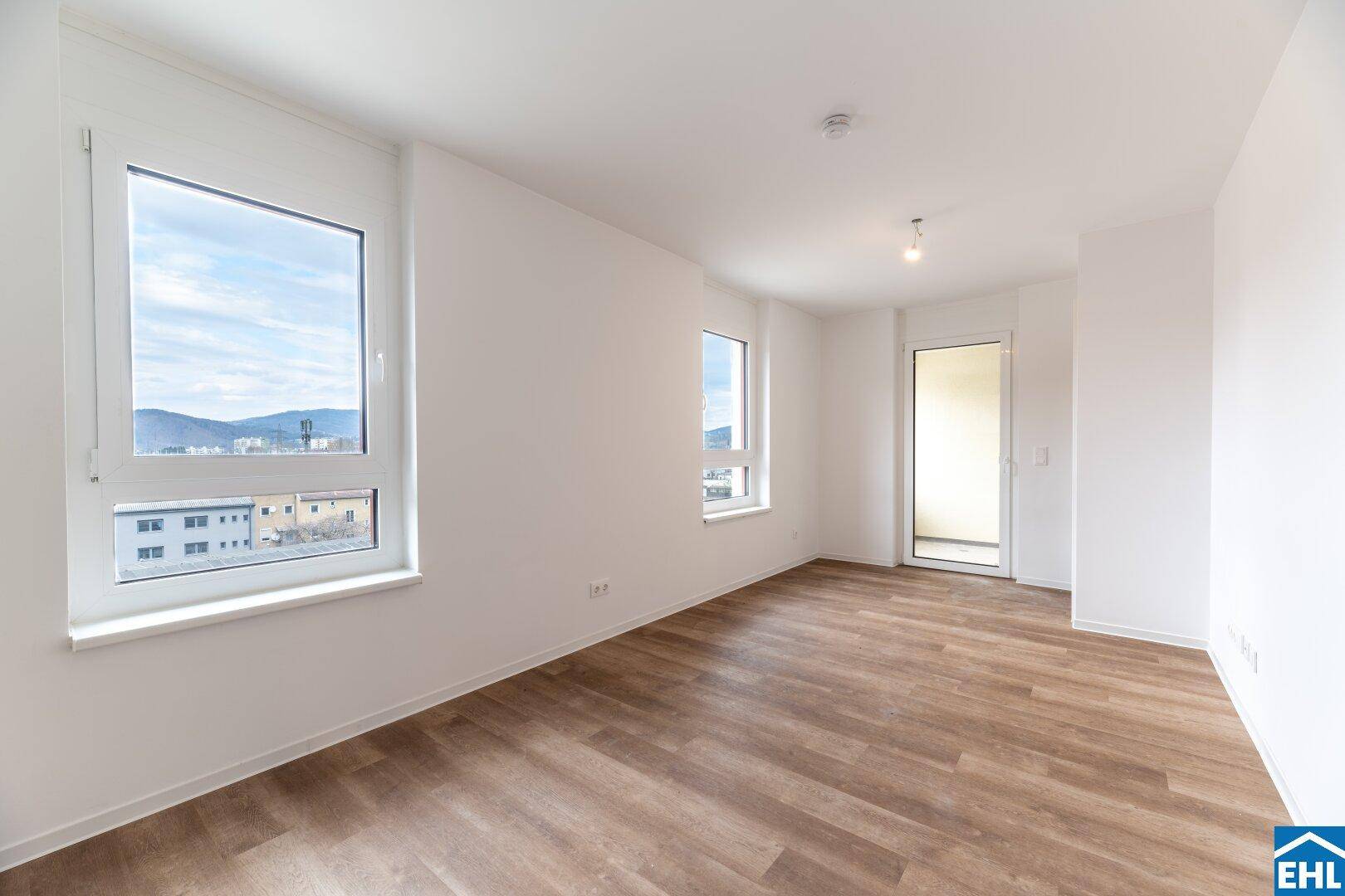 Helles Wohnzimmer mit modernem Laminatboden und Zugang zum Balkon, bietet viel natürliches Licht.