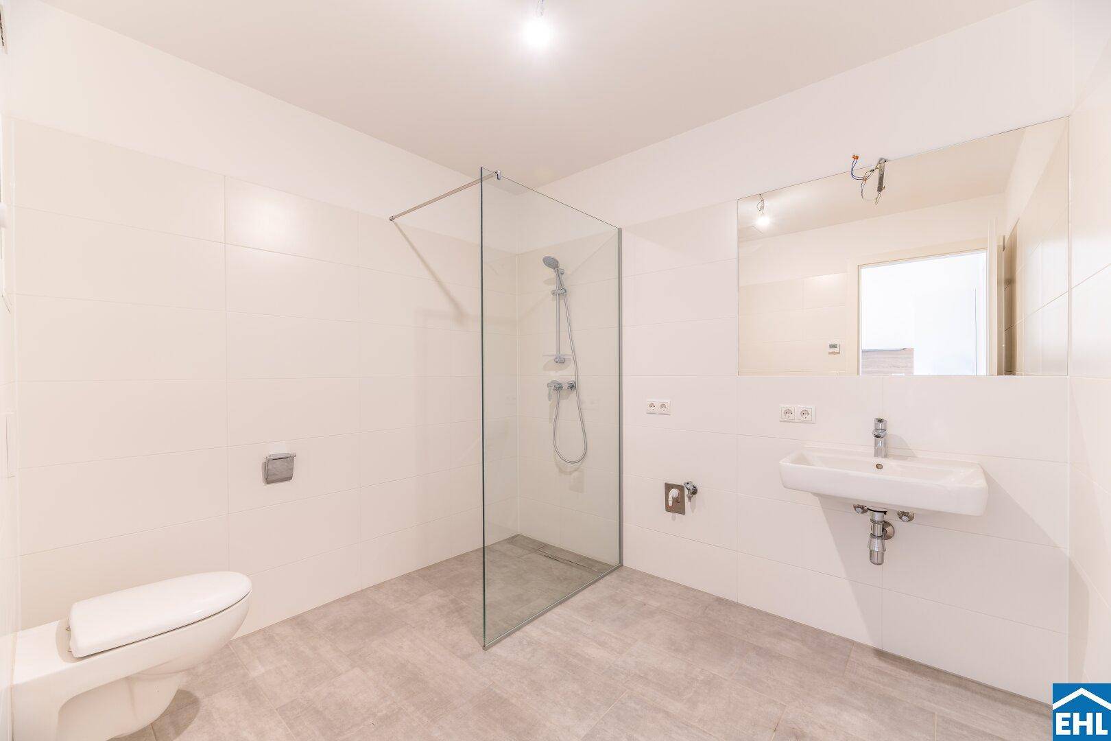 Modernes Badezimmer mit ebenerdiger Dusche, WC und großen weißen Fliesen.