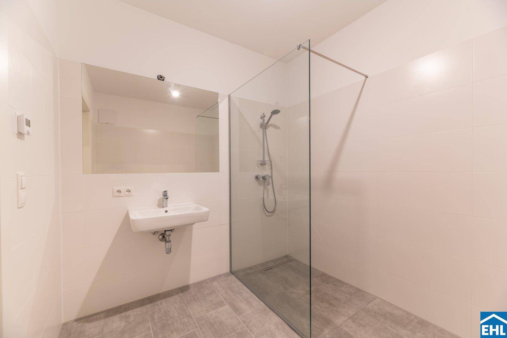 Modernes Badezimmer mit ebenerdiger Dusche, Waschbecken und großen Fliesen.