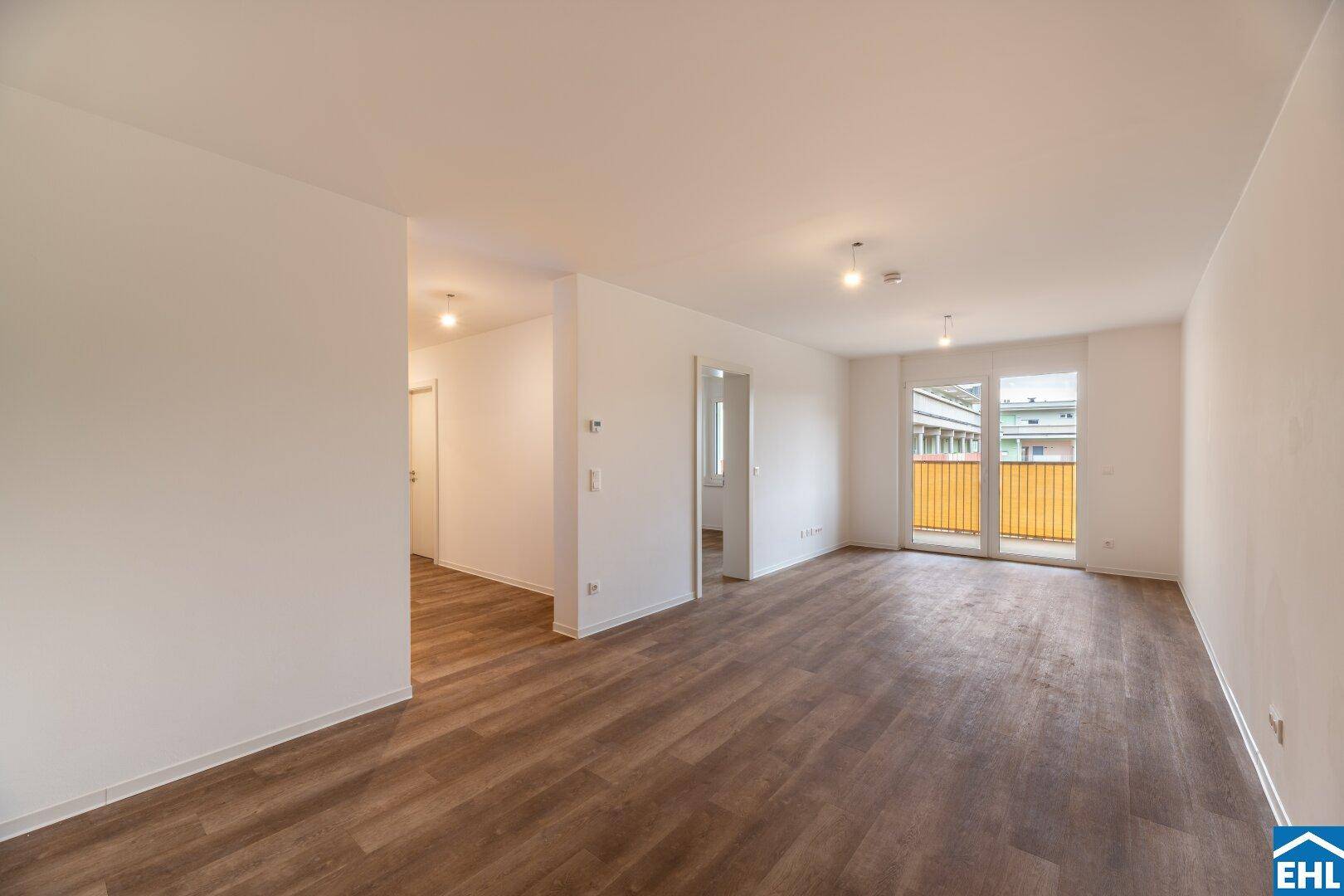 Heller, leerer Wohnbereich mit modernem Laminatboden und Zugang zum Balkon.