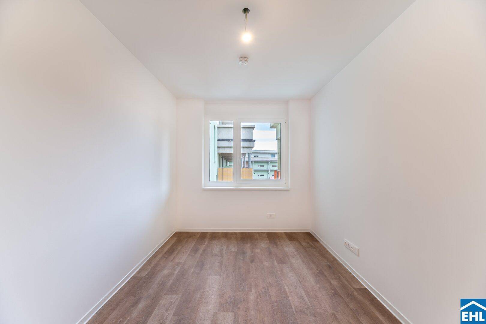 Leeres Zimmer mit Laminatboden und Fenster, ideal als Schlaf- oder Arbeitszimmer.