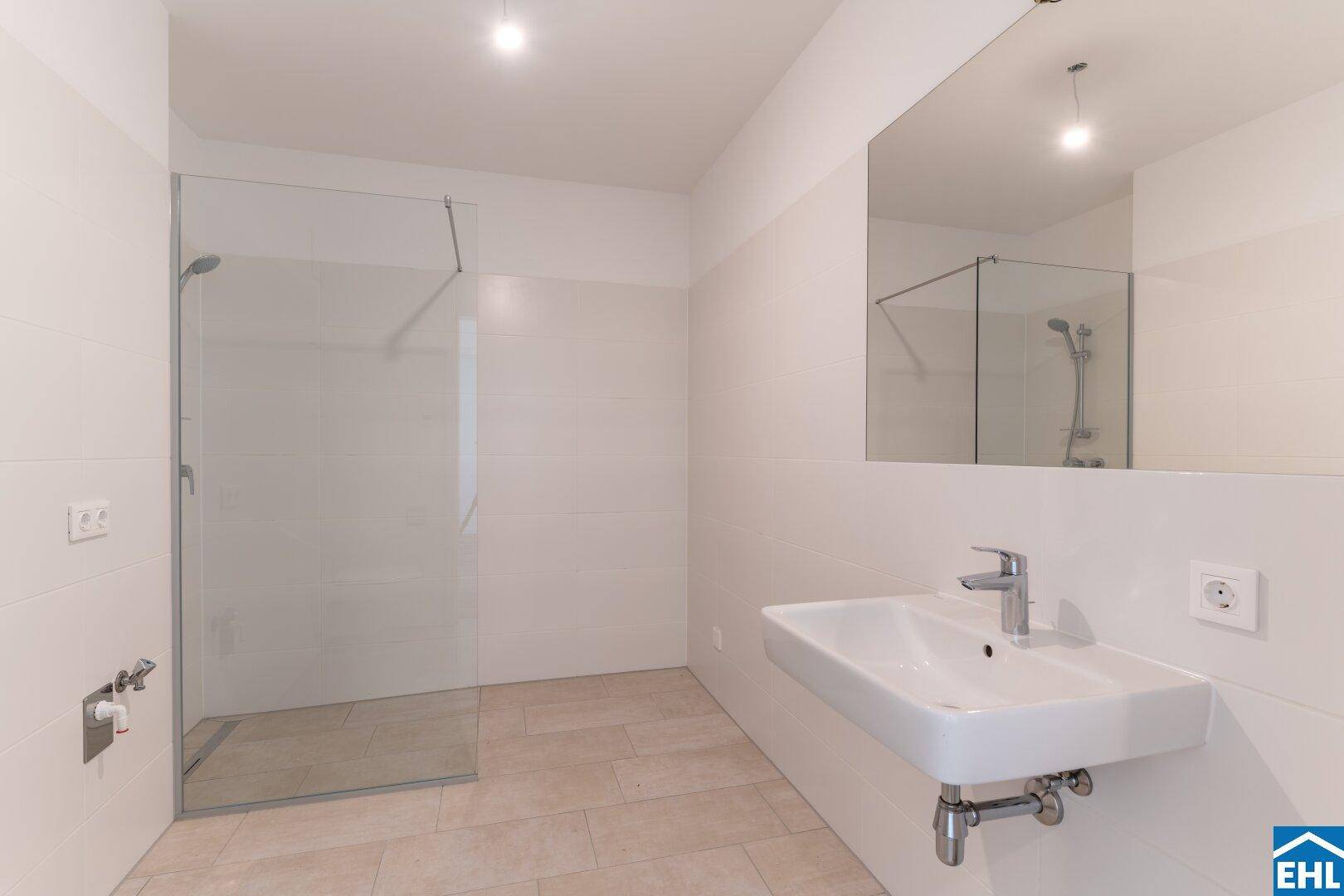 Modernes Badezimmer mit ebenerdiger Dusche, großem Spiegel und hellem Fliesenboden.
