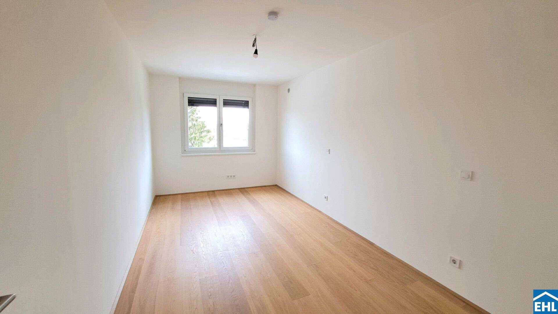 Leeres, helles Zimmer mit weiß gestrichenen Wänden und einem warmen Holzfußboden.