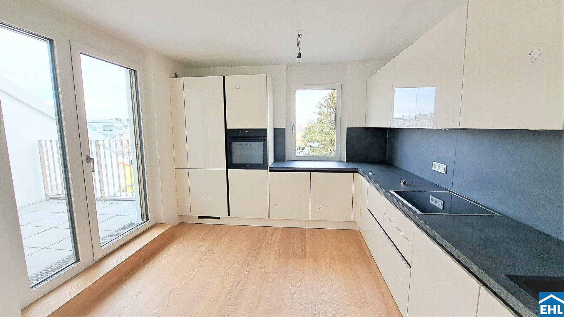 Moderne Einbauküche mit weißen Hochglanzfronten, dunkler Arbeitsplatte und Zugang zur Terrasse.
