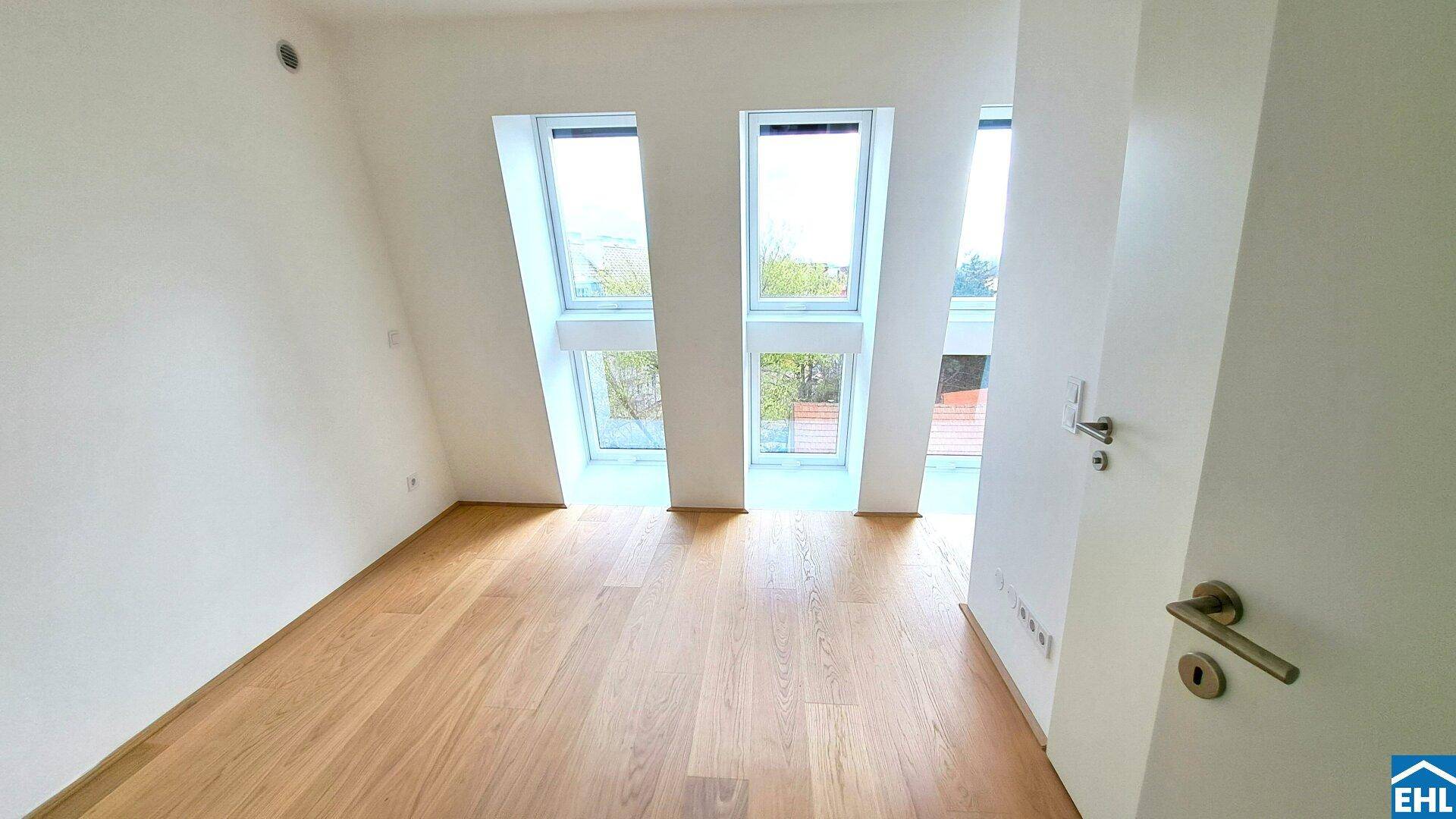 Helles Zimmer mit Dachschräge, großen Fenstern und hochwertigem Parkettboden.