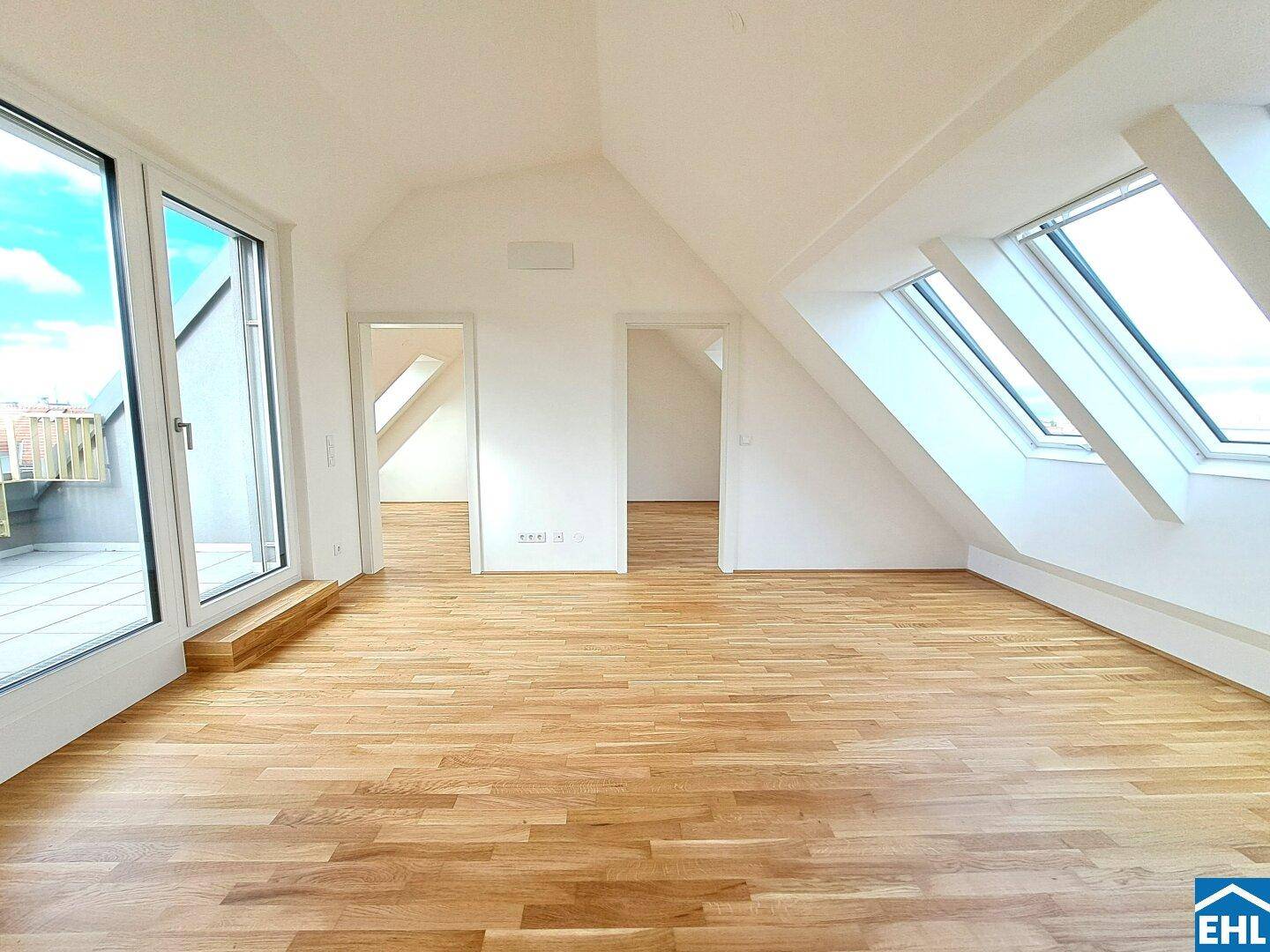 Helles Dachgeschosszimmer mit Holzboden, großen Fenstern und Zugang zu einer Terrasse.