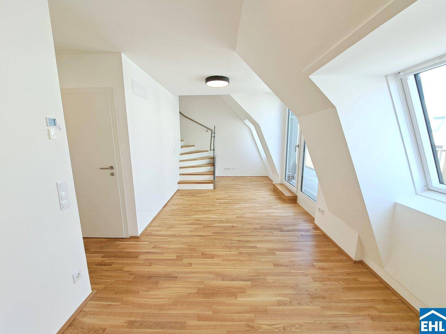 Offener Wohnbereich mit Holztreppe, großen Fenstern und Dachschrägen.
