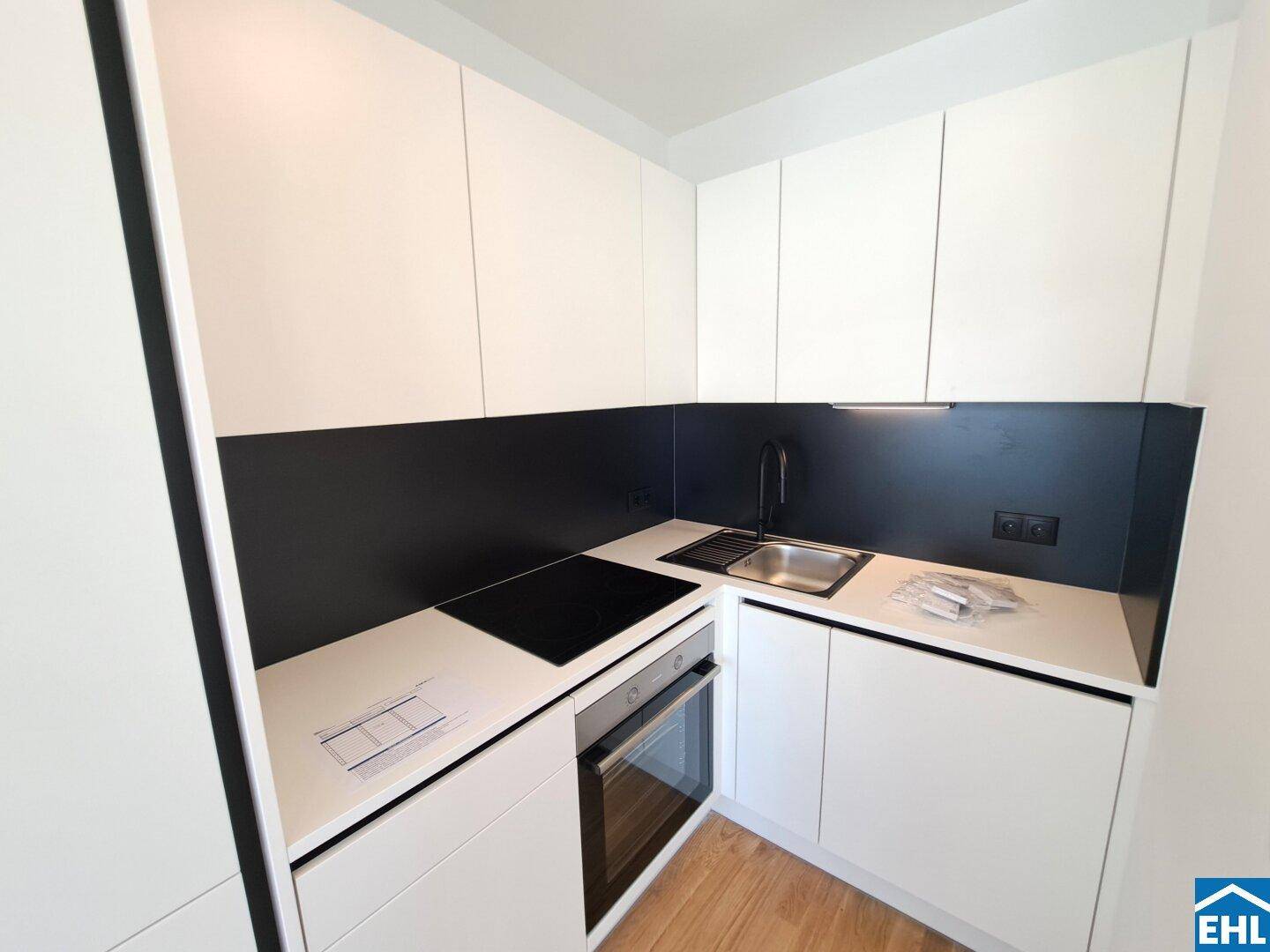 Moderne Einbauküche mit weißen Schränken, schwarzer Rückwand und Induktionskochfeld.