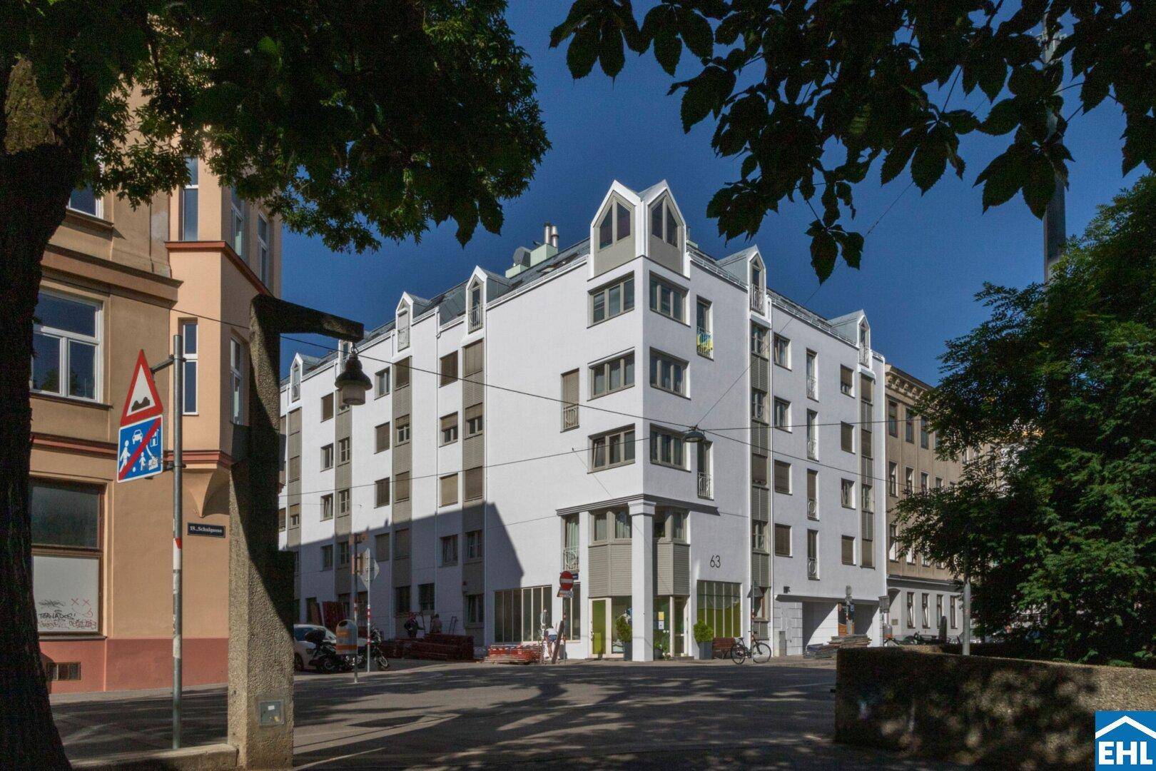 Modernes Gebäude mit weißer Fassade, grauen Akzenten und markanten Dachgauben an einer Straßenecke.