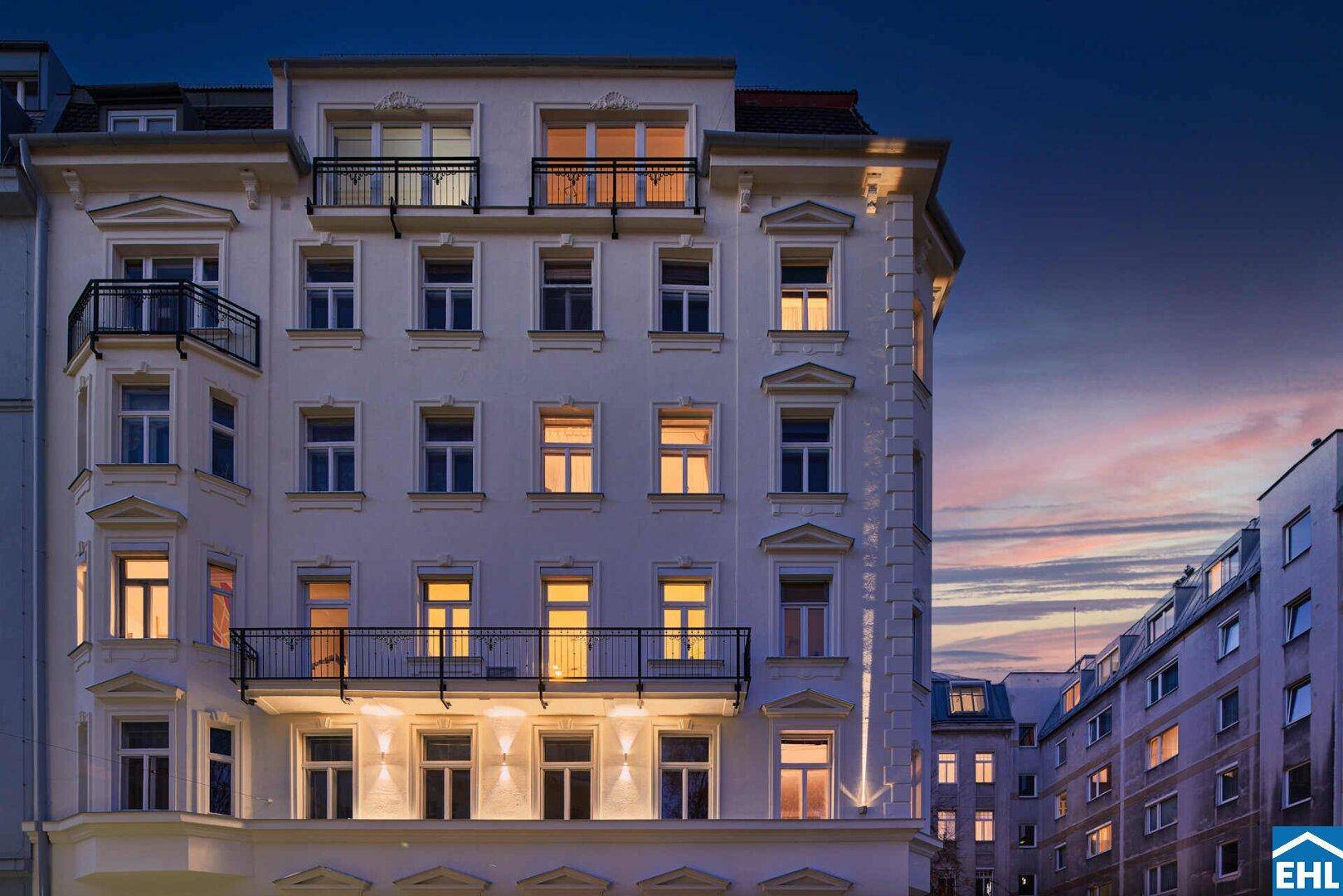 Historisches Gebäude mit beleuchteten Fenstern und Balkonen in der Abenddämmerung.