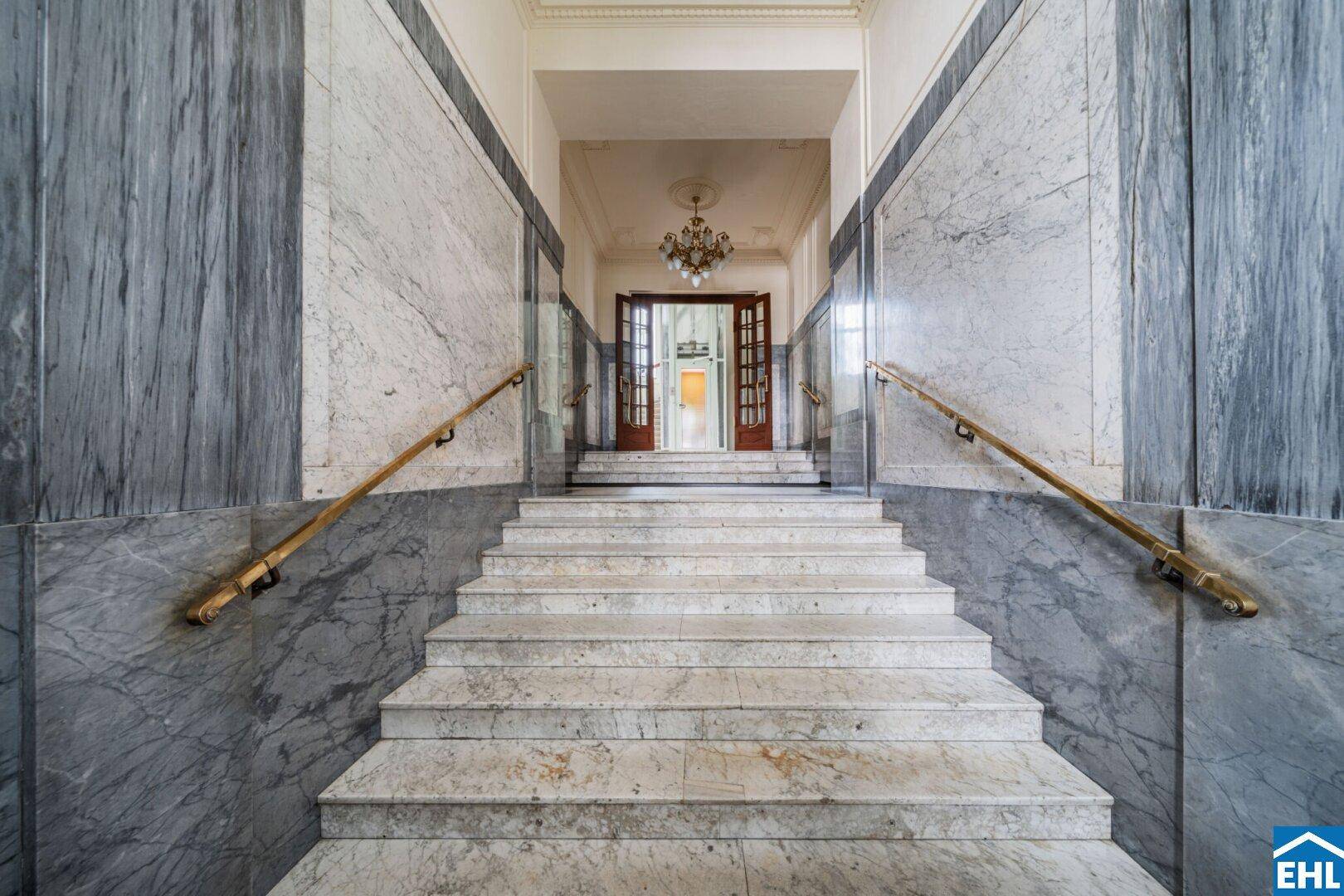 Repräsentatives Treppenhaus mit Marmorstufen, eleganten Handläufen und einem klassischen Kronleuchter.