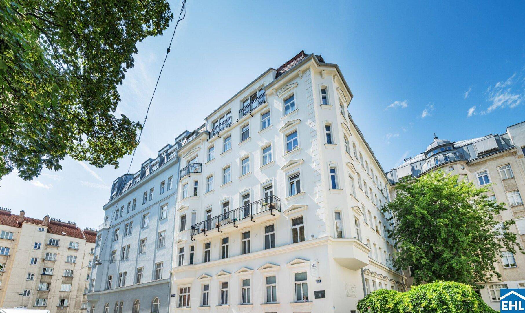 Klassisches weißes Gebäude mit vielen Fenstern und kleinen Balkonen unter blauem Himmel.