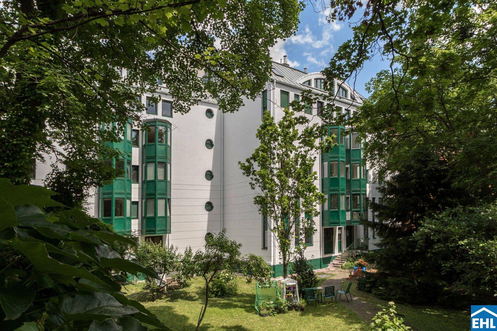 Gebäudefassade vom grünen Garten aus gesehen, umgeben von dichtem Baumbestand.