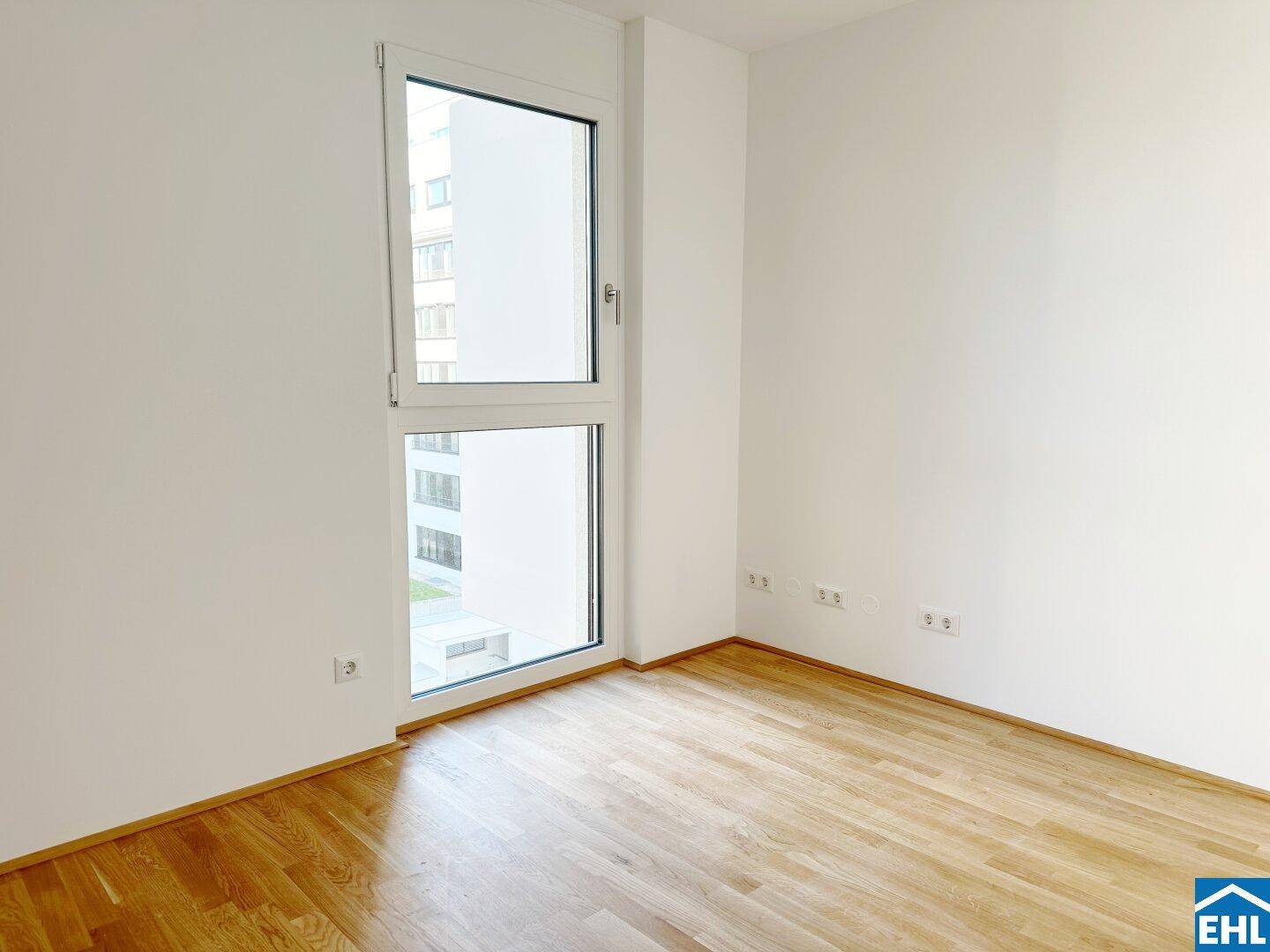 Heller, leerer Raum mit großem Fenster und Holzfußboden, bietet vielseitige Nutzungsmöglichkeiten.