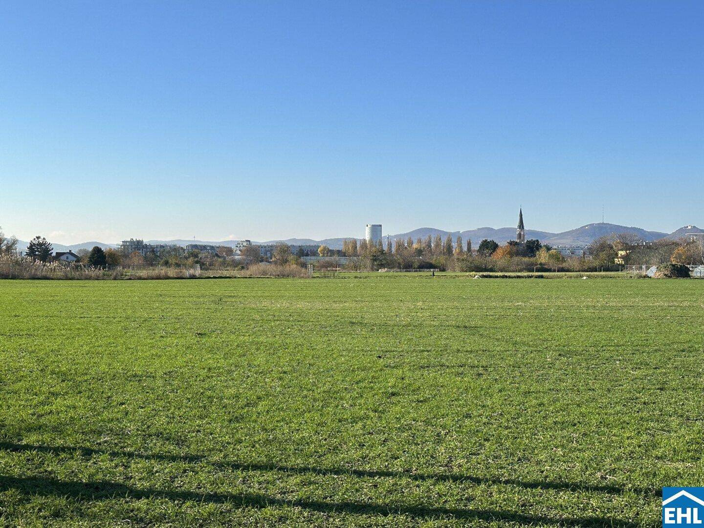 Weitläufiges grünes Feld mit Blick auf die Stadt und Berge in der Ferne.