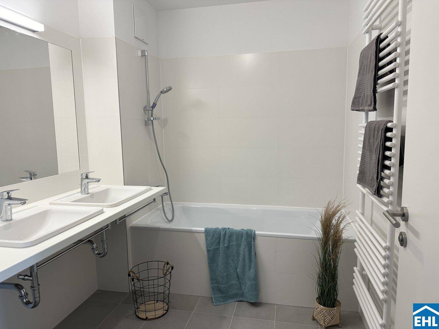 Modernes Badezimmer mit Doppelwaschbecken, Badewanne und beheiztem Handtuchhalter.