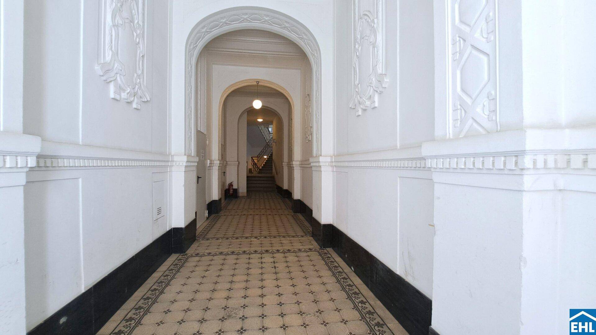 Historischer Eingangsbereich mit hohen Gewölbebögen, gemustertem Fliesenboden und dekorativen Elementen.