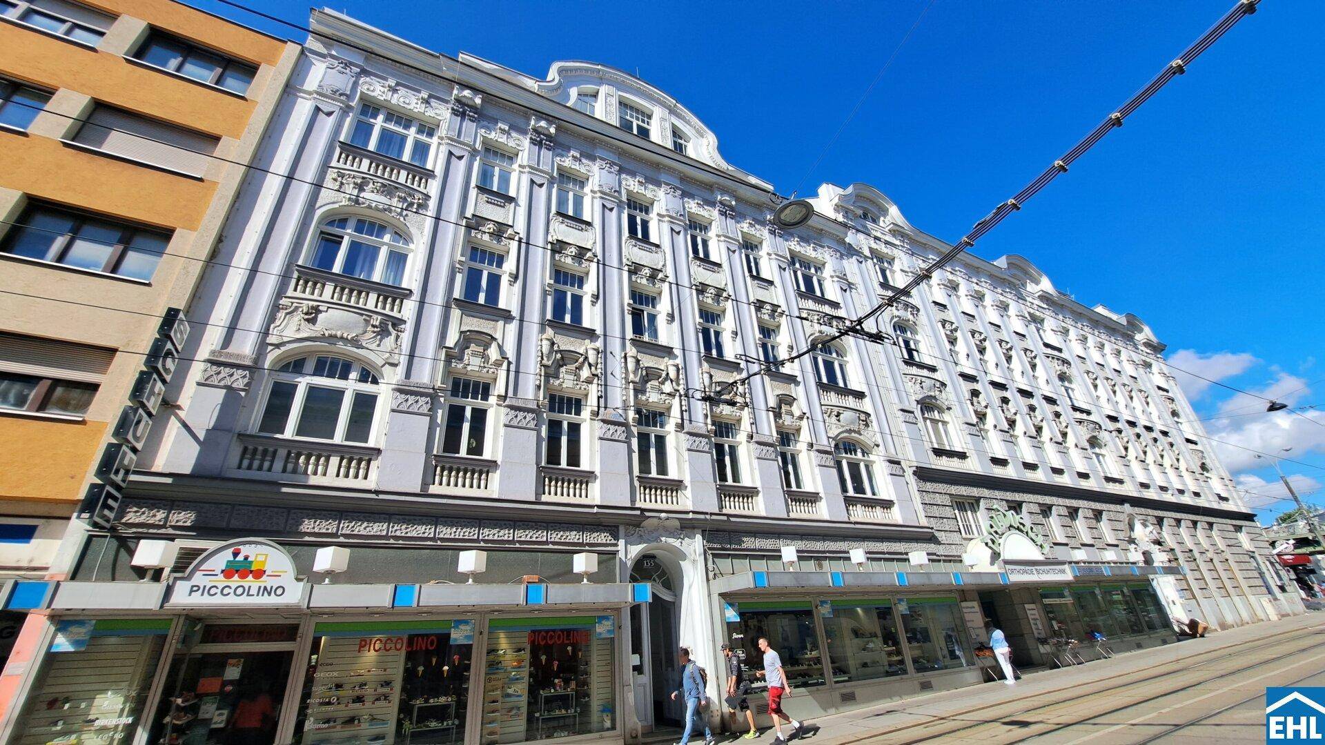 Prächtige Altbaufassade mit reich verzierten Details und Geschäften im Erdgeschoss an einer Straße.