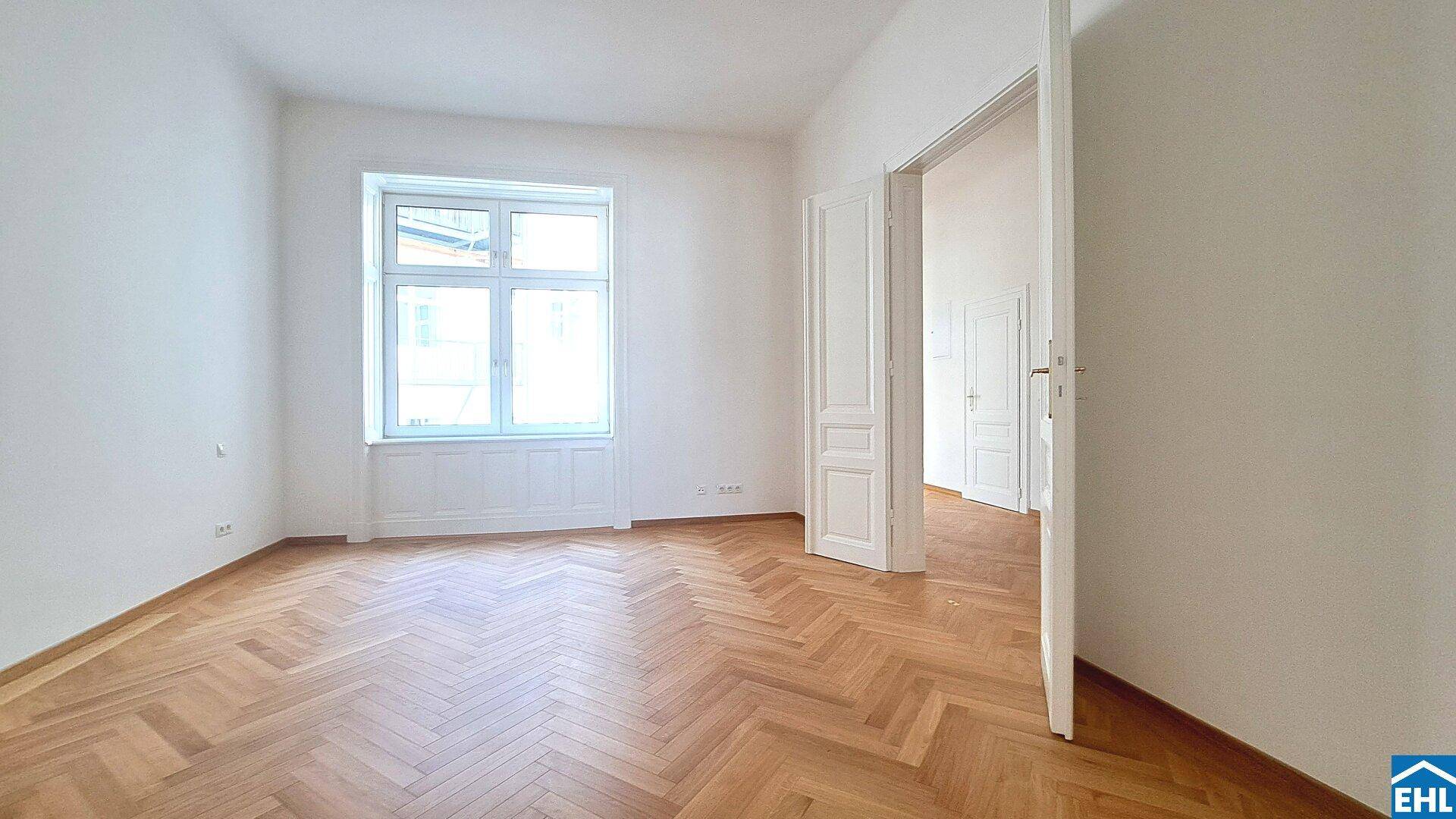 Geräumiges Zimmer mit klassischem Fischgrätparkett und großen Fenstern, die den Raum erhellen.
