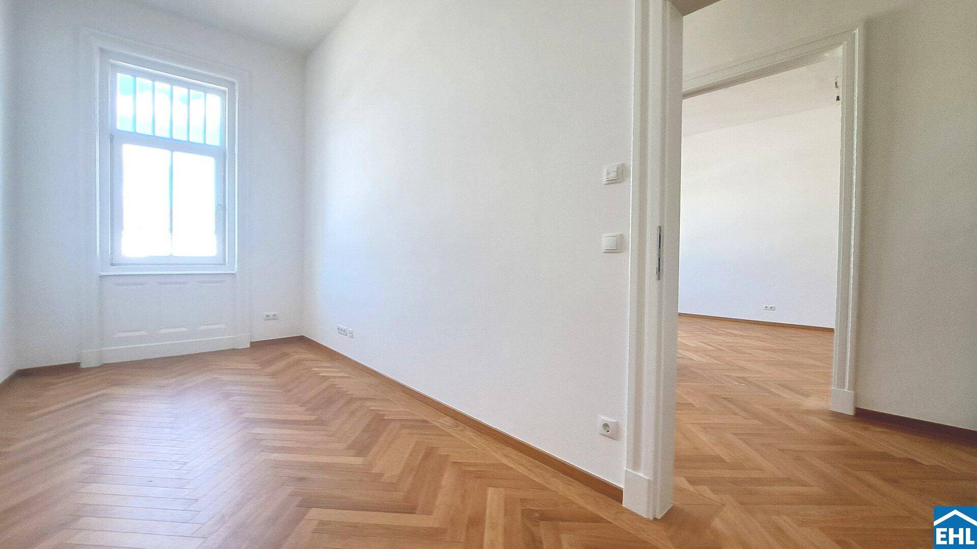 Heller Raum mit traditionellem Fischgrätparkett und großen Fenstern, die eine angenehme Atmosphäre schaffen.