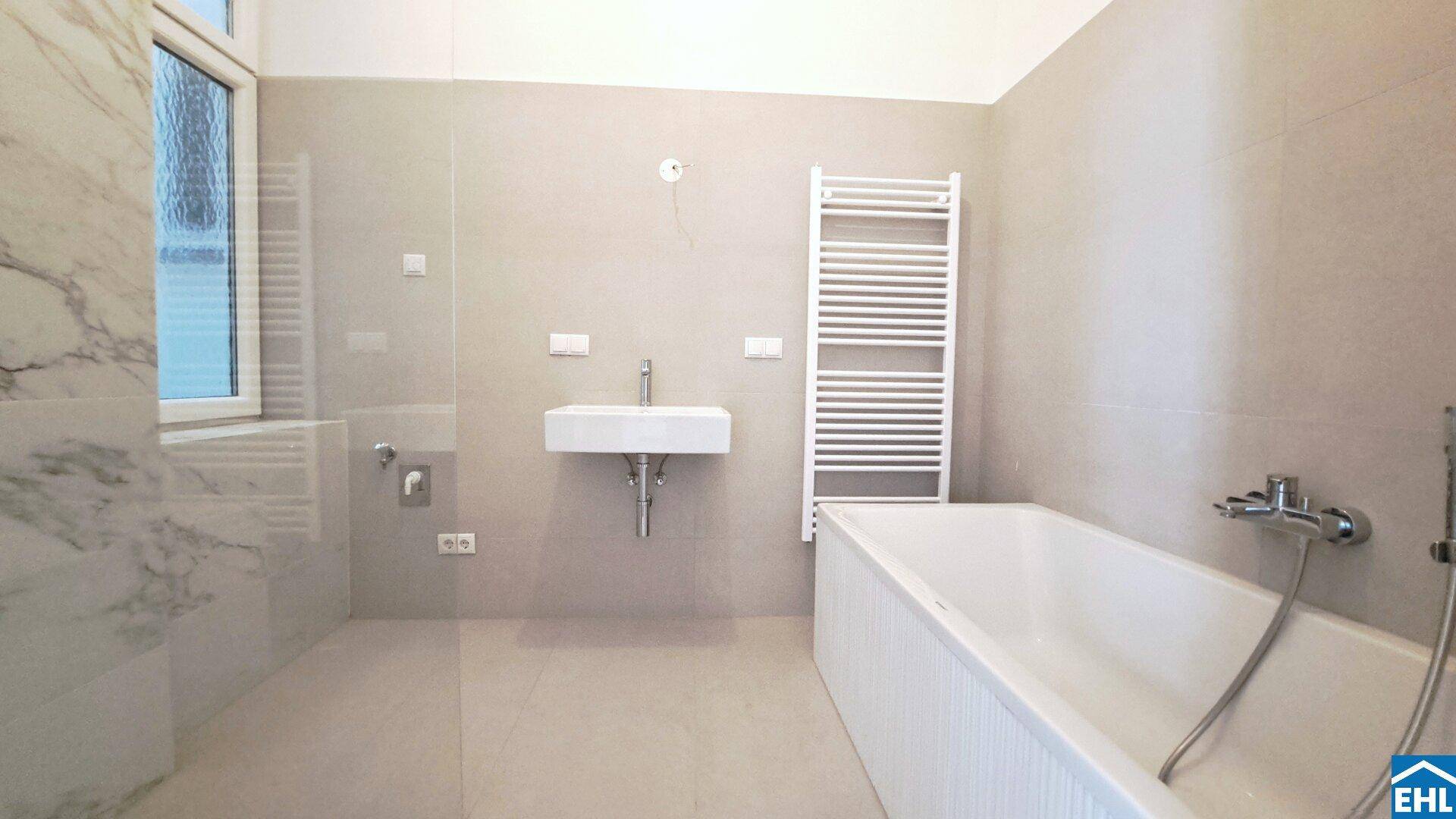 Modernes Badezimmer mit Badewanne, Wandwaschbecken, beheiztem Handtuchhalter und Fenster.