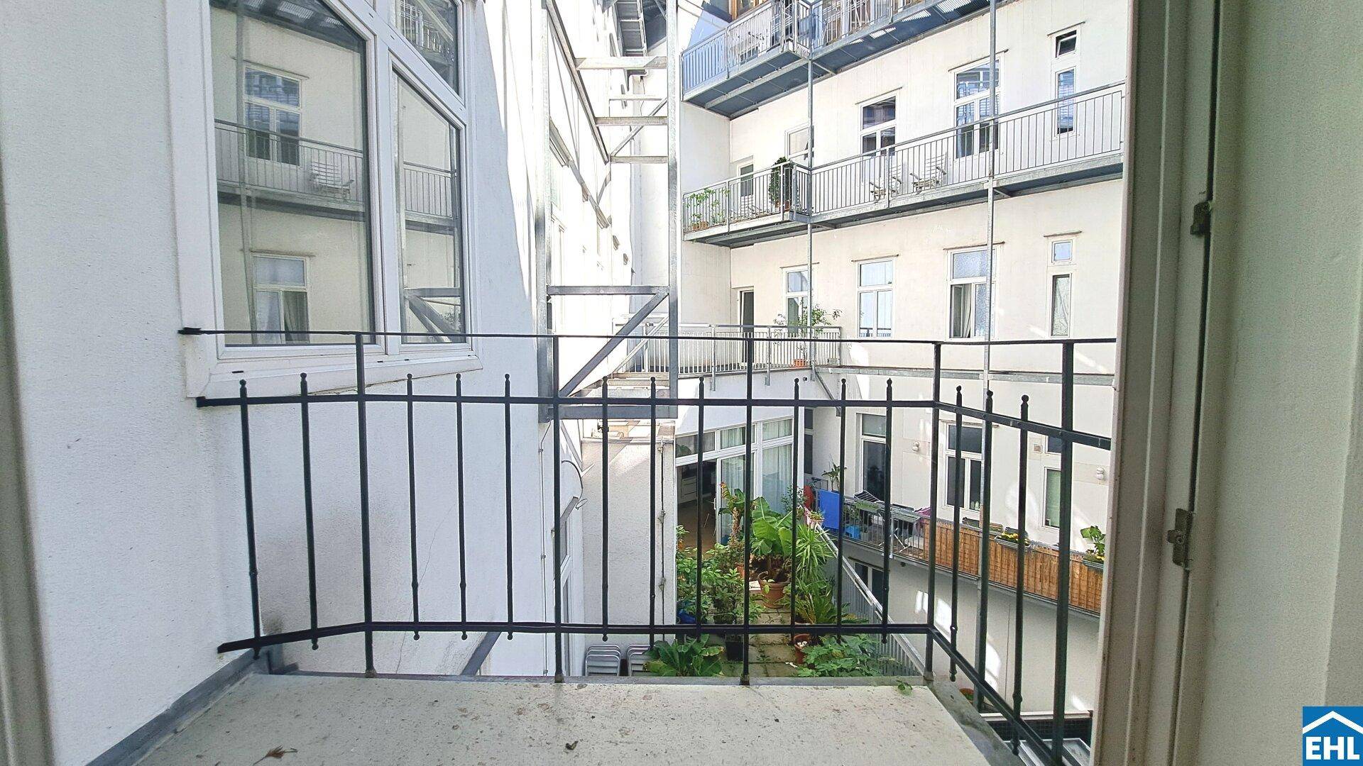 Kleiner Balkon mit schmiedeeisernem Geländer und Blick auf einen begrünten Innenhof.