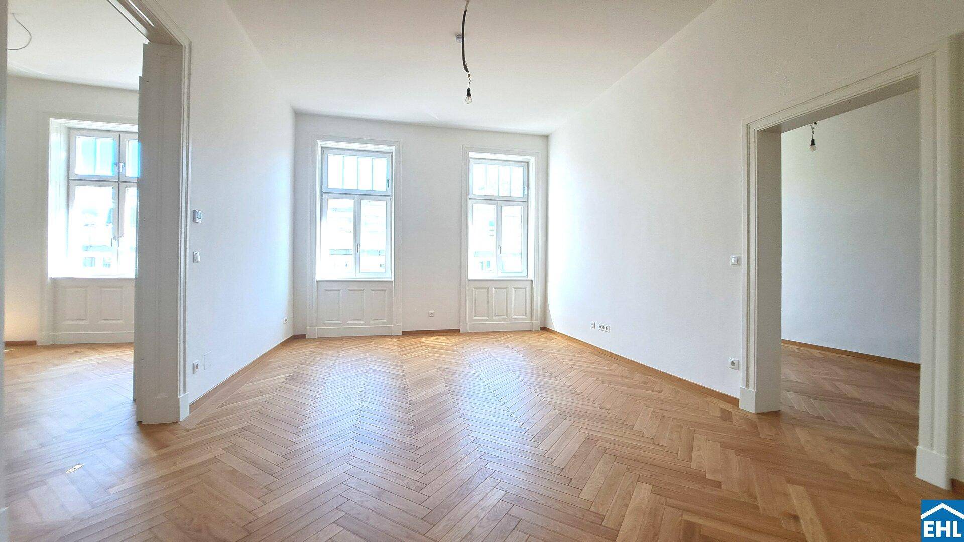 Lichtdurchfluteter Raum mit klassischem Fischgrätparkett und zwei hohen Fenstern.