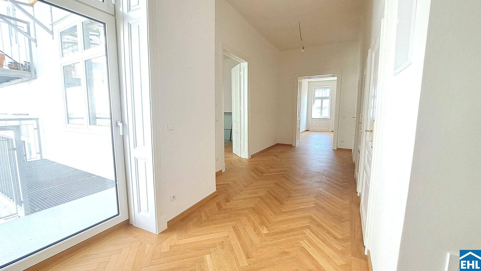 Heller Flur mit Fischgrätparkett und Zugang zu verschiedenen Räumen sowie einem Balkon.