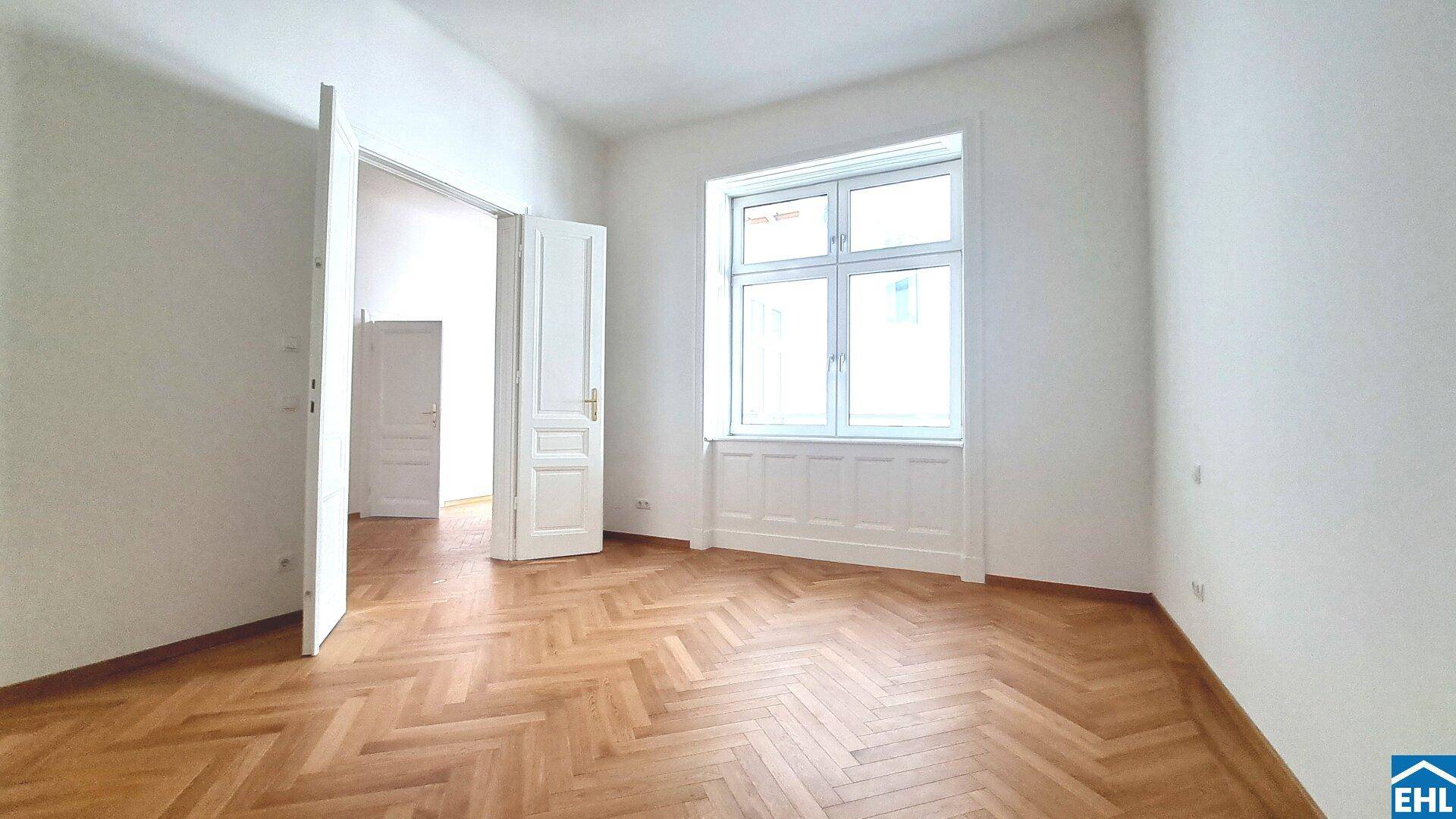 Heller Raum mit Fischgrätparkett und einem großen Fenster, das den Raum erhellt.
