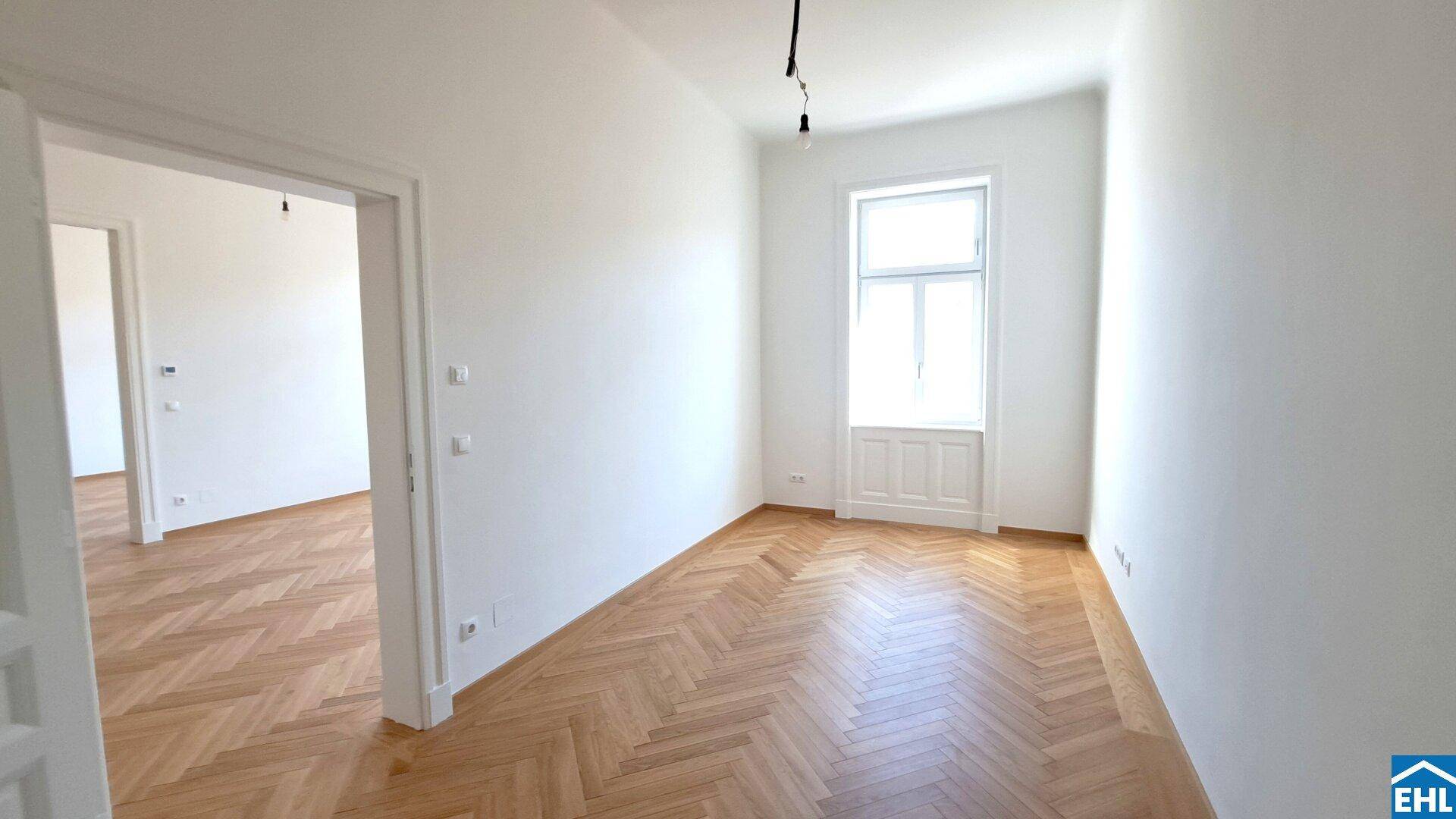 Leeres Zimmer mit Fischgrätparkett und einem hohen Fenster, das für viel Helligkeit sorgt.