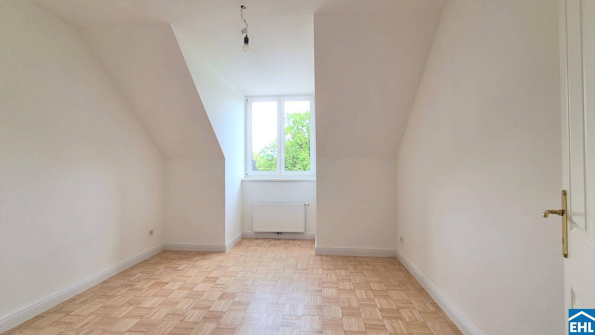 Gemütliches Zimmer im Dachgeschoss mit Parkettboden, weiß gestrichenen Wänden und Blick ins Grüne.