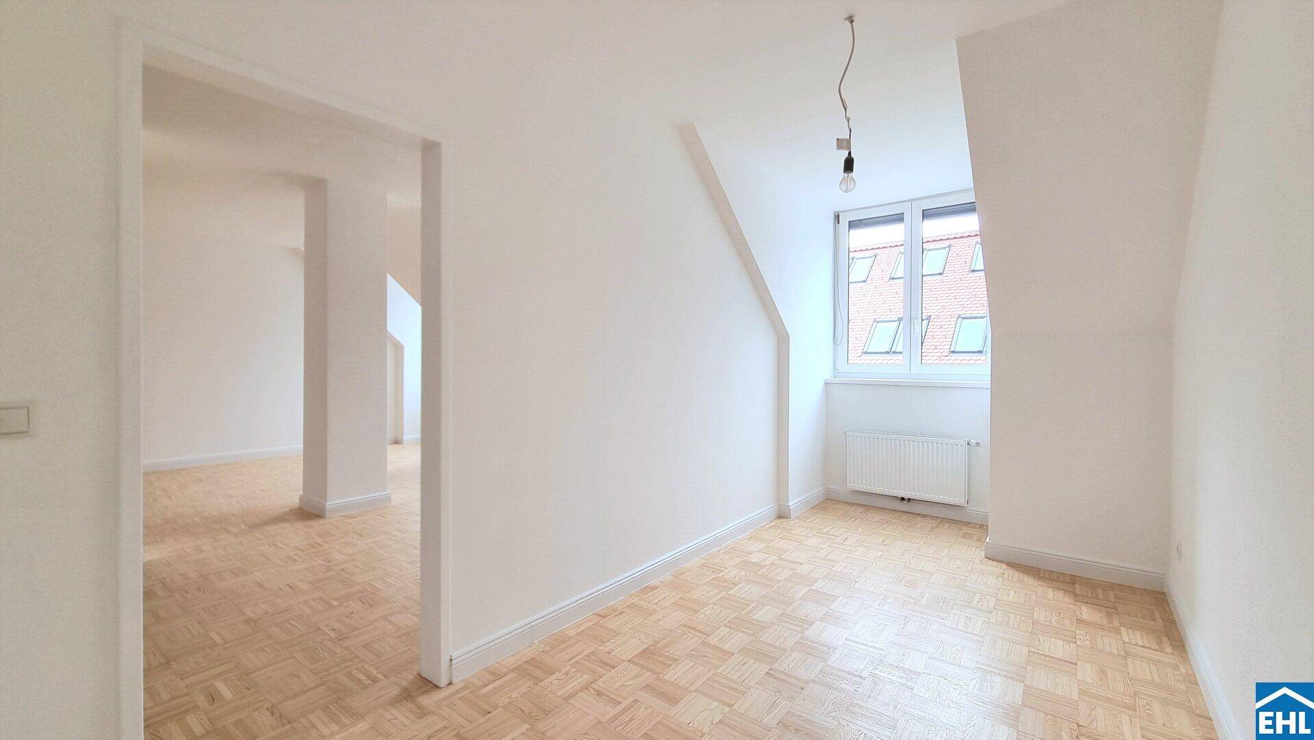 Helles Dachgeschosszimmer mit Parkettboden, schrägen Wänden und einem Fenster mit Blick nach draußen.