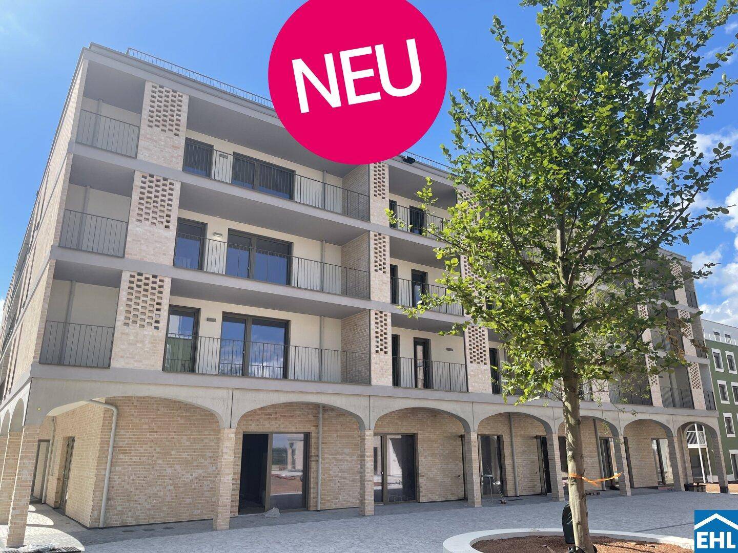 Modernes Mehrfamilienhaus mit Balkonen und Arkaden im Erdgeschoss, als Neubau gekennzeichnet.