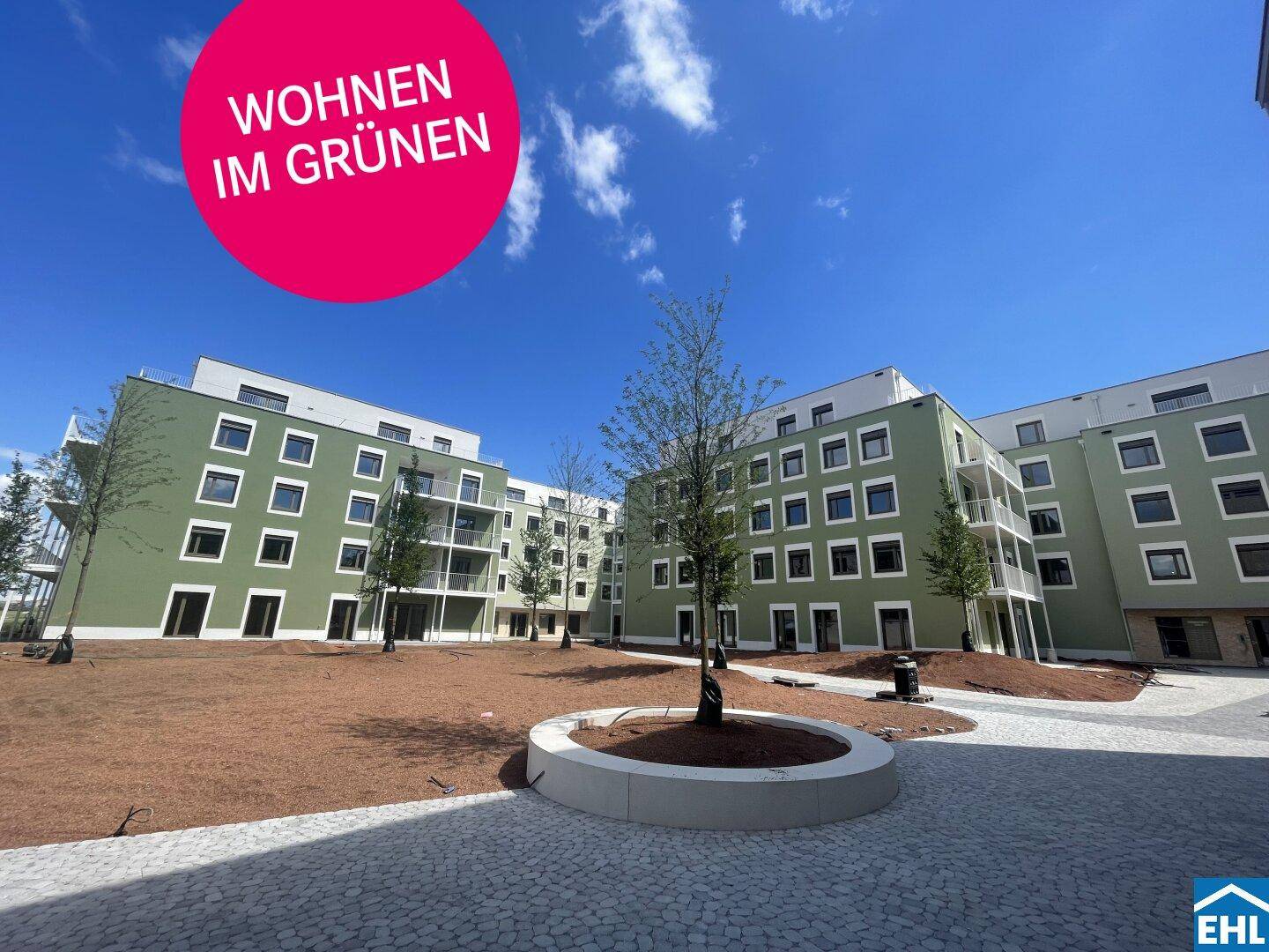 Moderne Wohnanlage mit grünen Fassaden und einem begrünten Innenhof unter blauem Himmel.