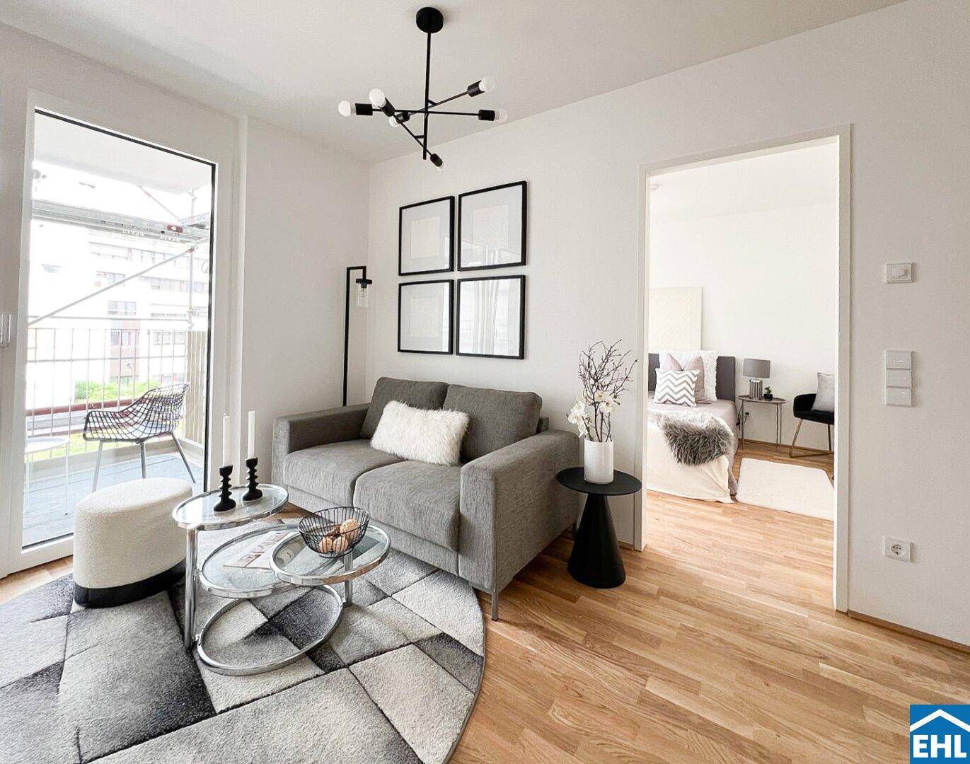 Helles, modern eingerichtetes Wohnzimmer mit Holzboden, Zugang zum Balkon und Blick ins Schlafzimmer.
