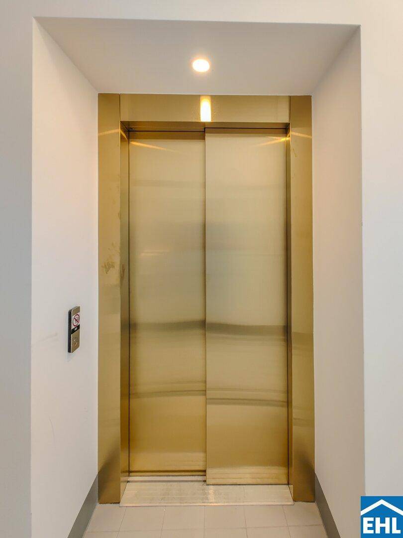 Eleganter Aufzug mit goldfarbenen Türen in einem hellen Flurbereich des Gebäudes.
