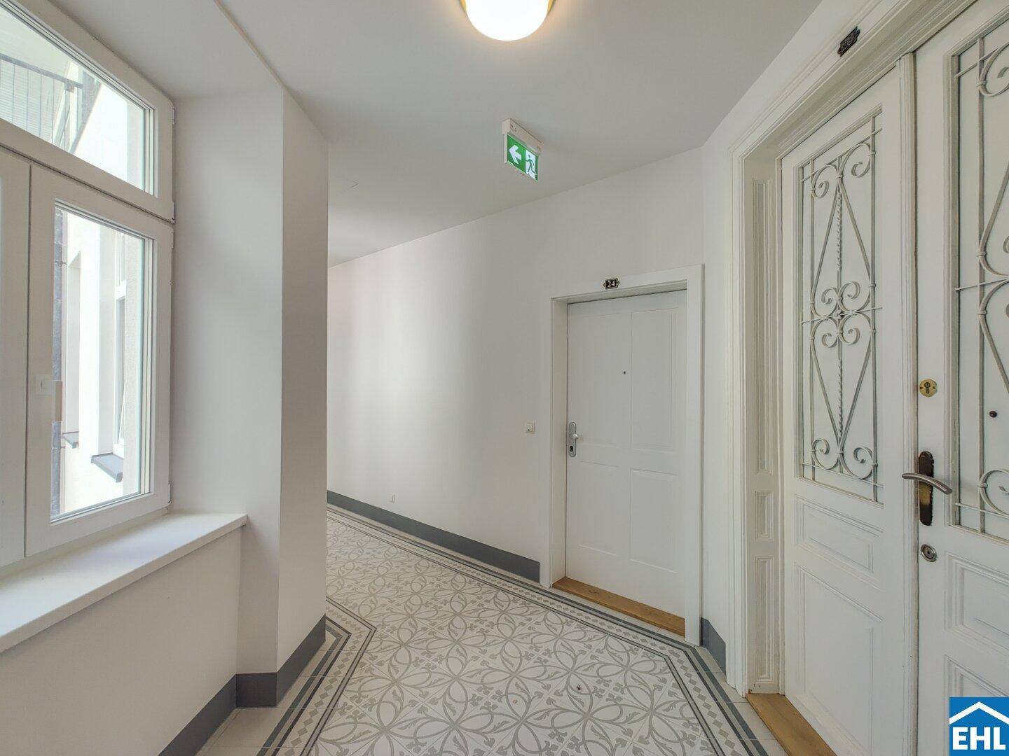 Historischer Flur mit gemusterten Fliesen und hohen Fenstern, typisch für Altbau.