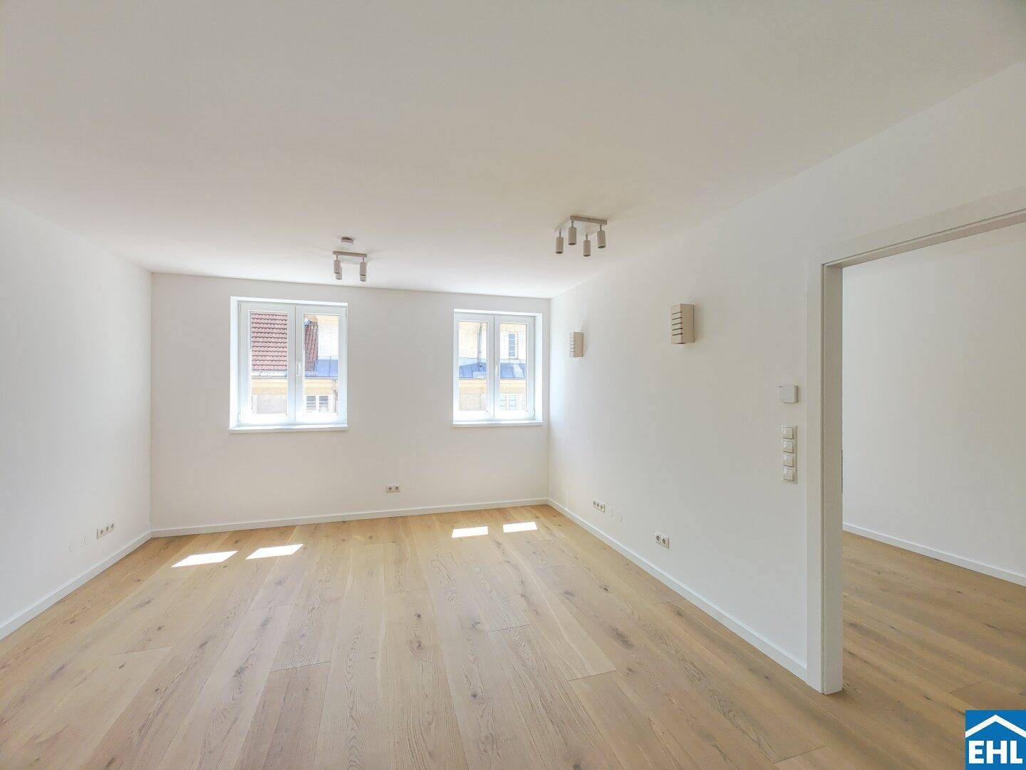 Lichtdurchfluteter Raum mit hellem Holzboden und zwei Fenstern, ideal als Schlafzimmer.