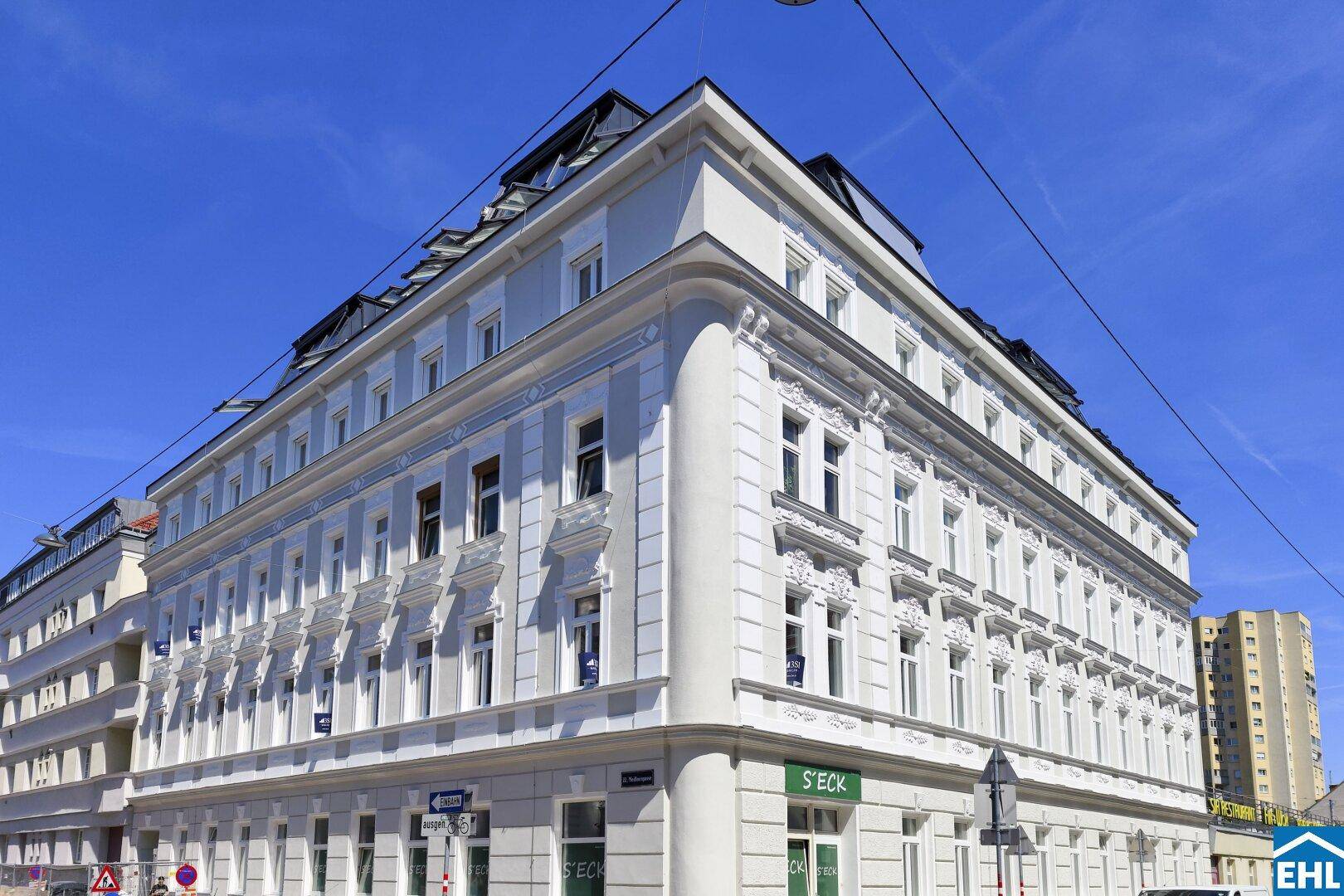 Historisches Eckgebäude mit eleganter Fassade und vielen Fenstern unter blauem Himmel.
